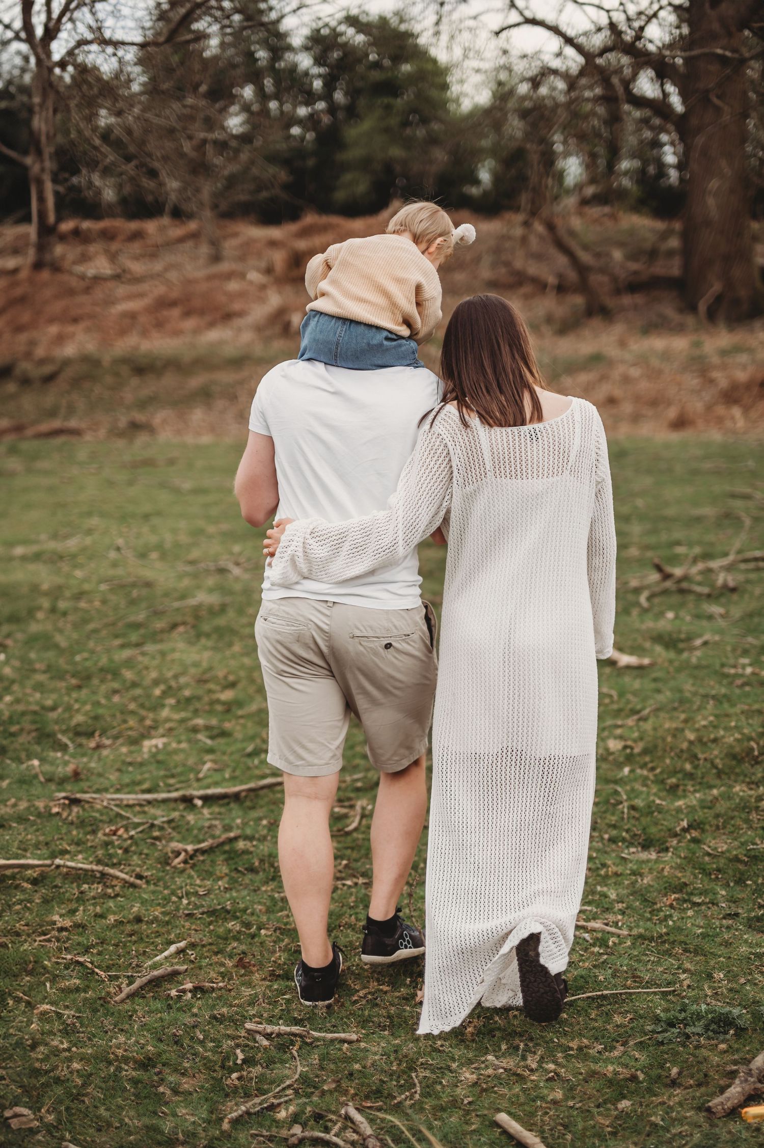 Family of three walking together through a scenic outdoor woodland setting.