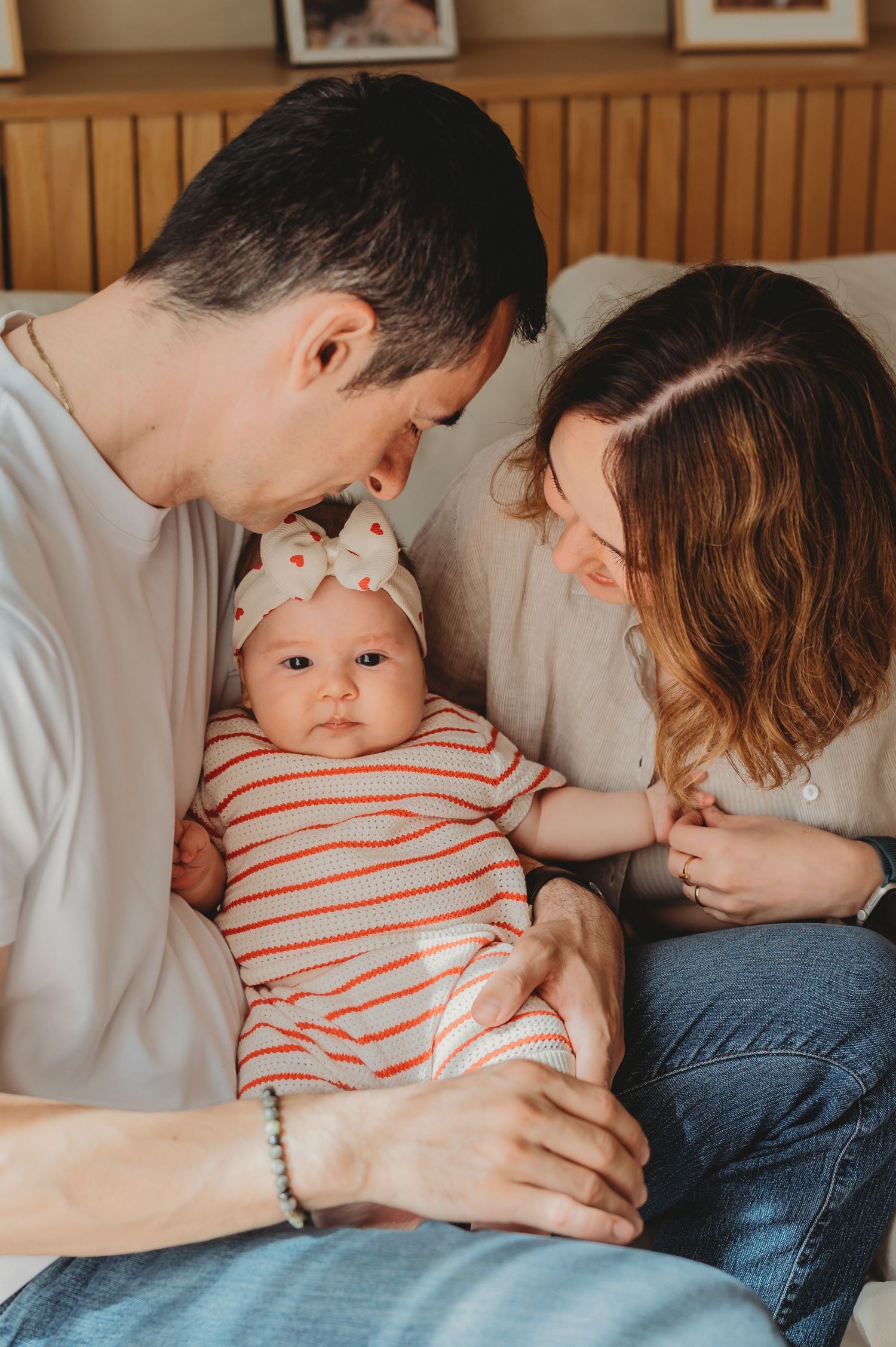 Happy parents sitting together on a couch lovingly gazing at their newborn baby girl.