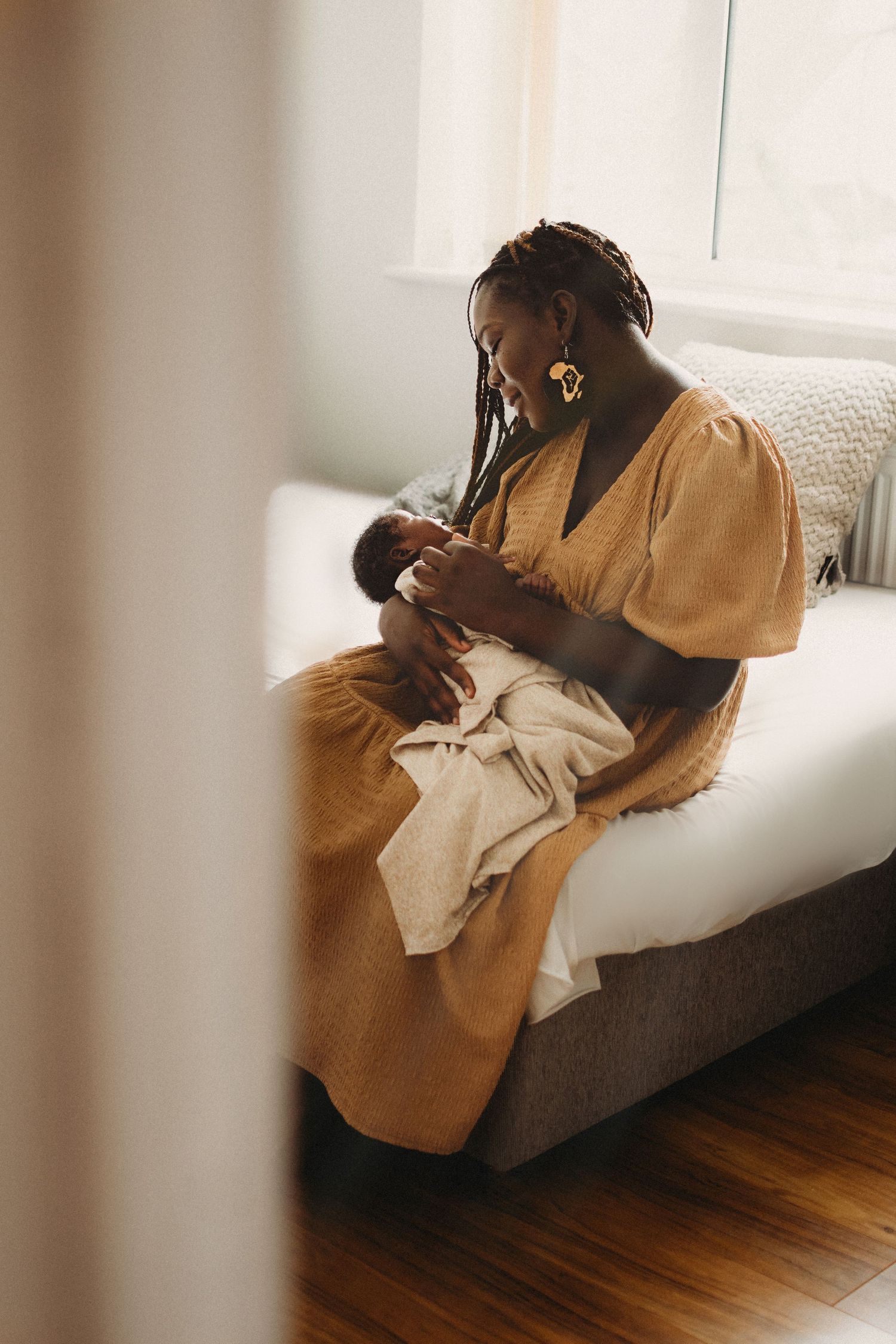 African American mother in yellow dress sitting on bed tenderly holding her newborn baby.