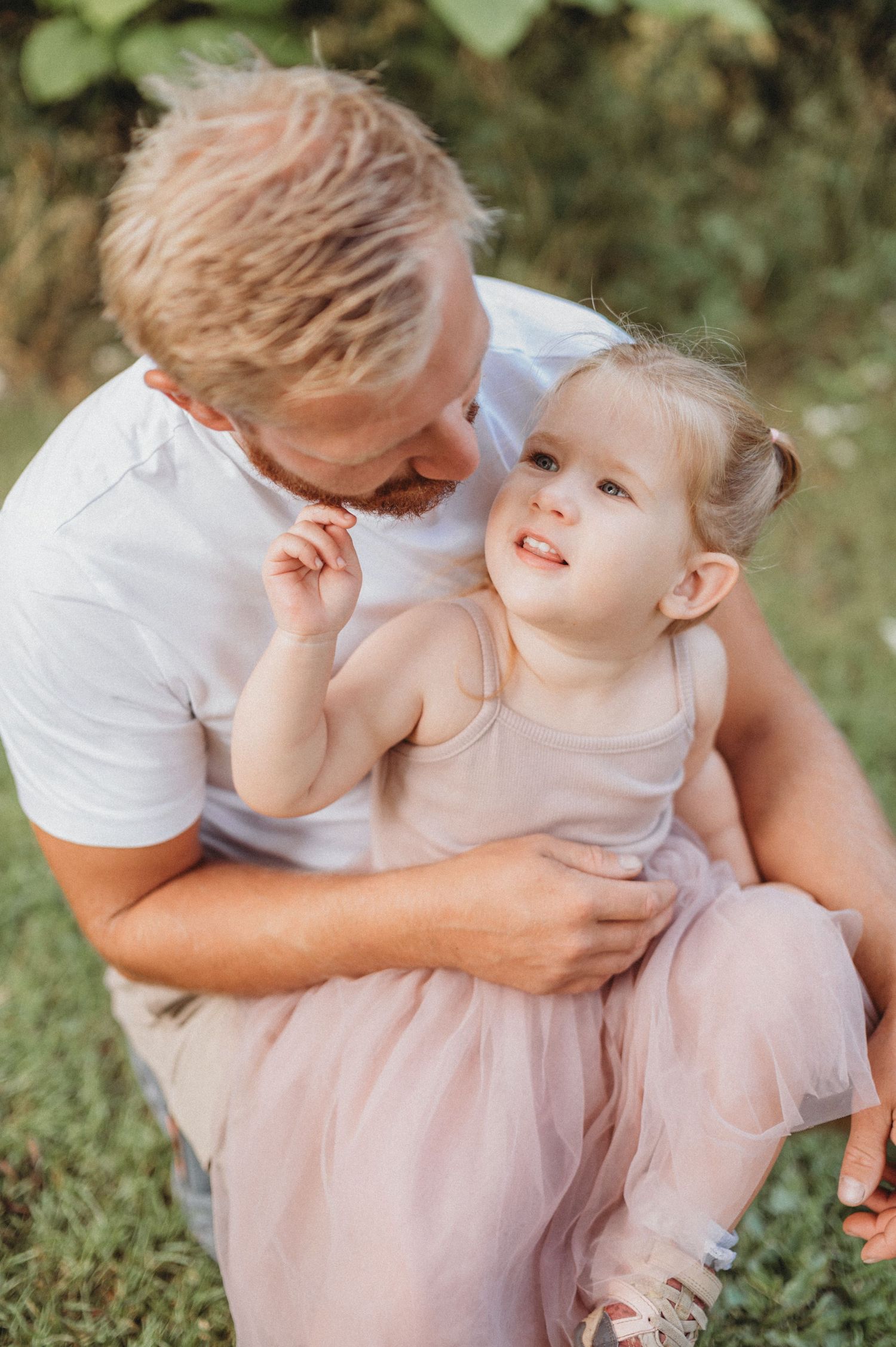 Loving father holding and whispering to his smiling toddler daughter outdoors in nature.