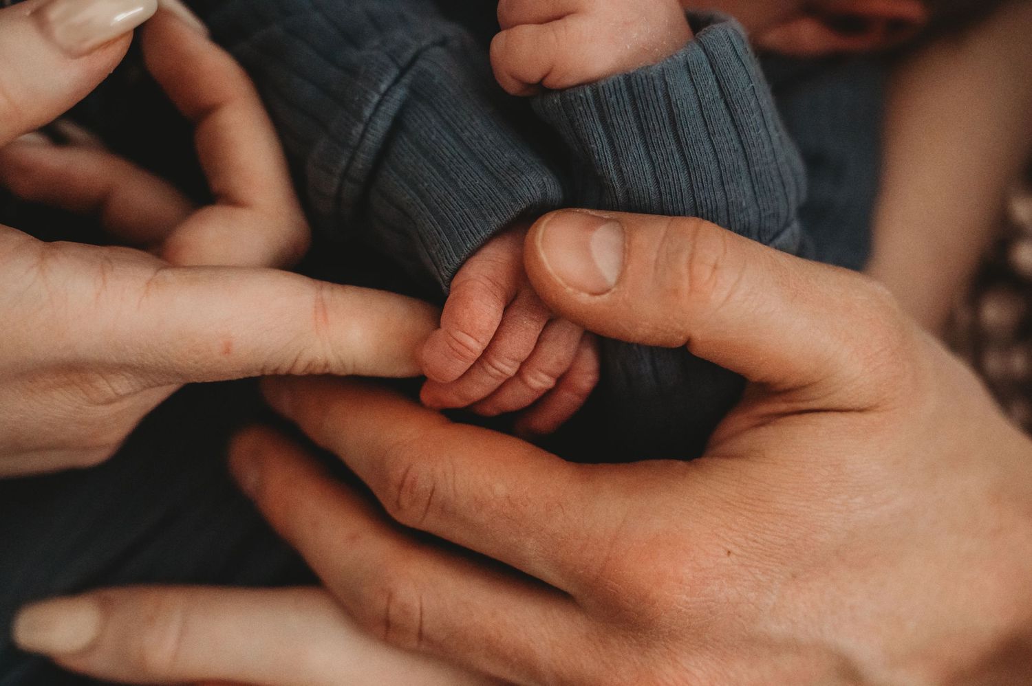 Newborn baby gripping parent's finger with tiny hand, close-up family bonding moment.