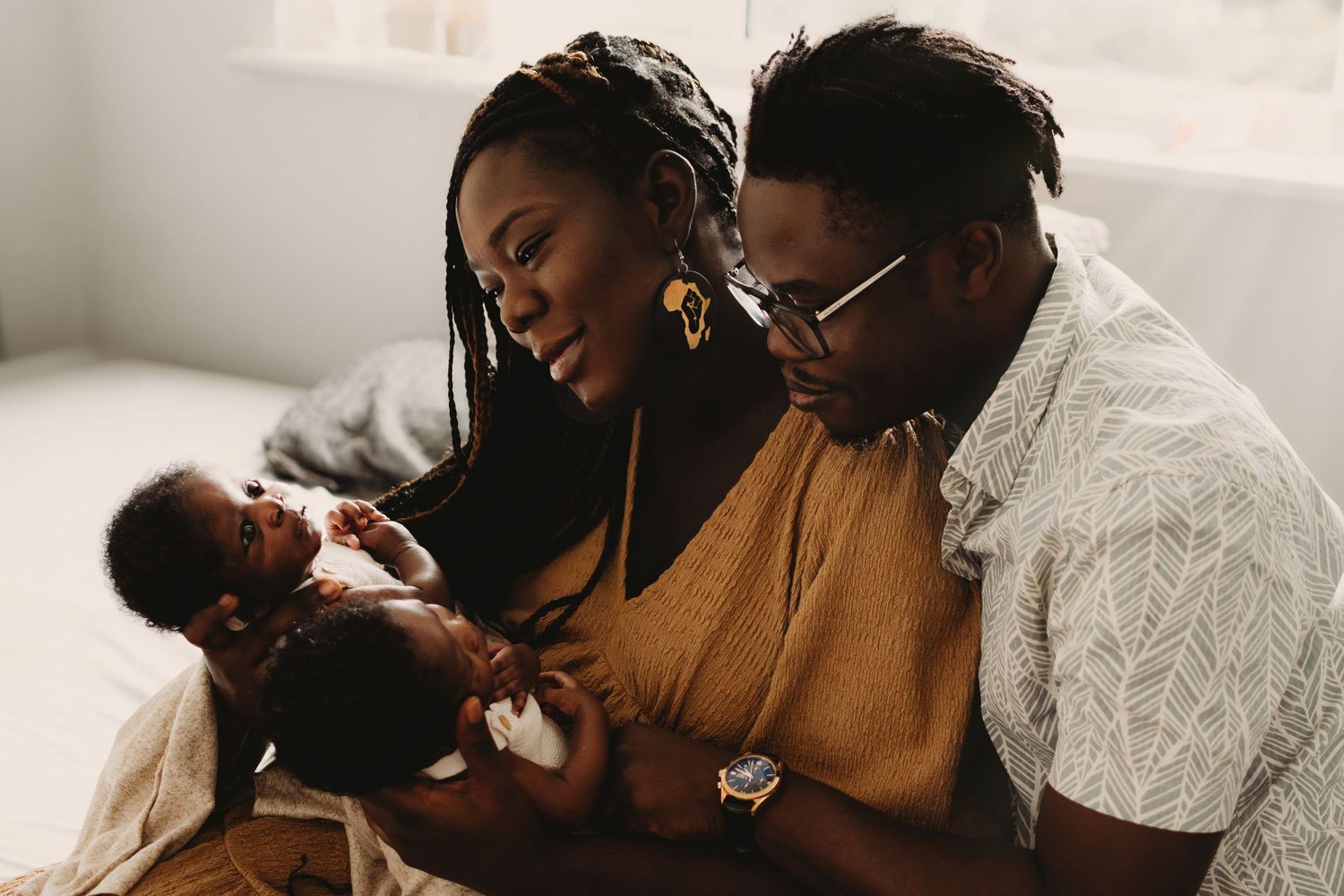 A couple lovingly gazes at their newborn twins in a warm, intimate family portrait.