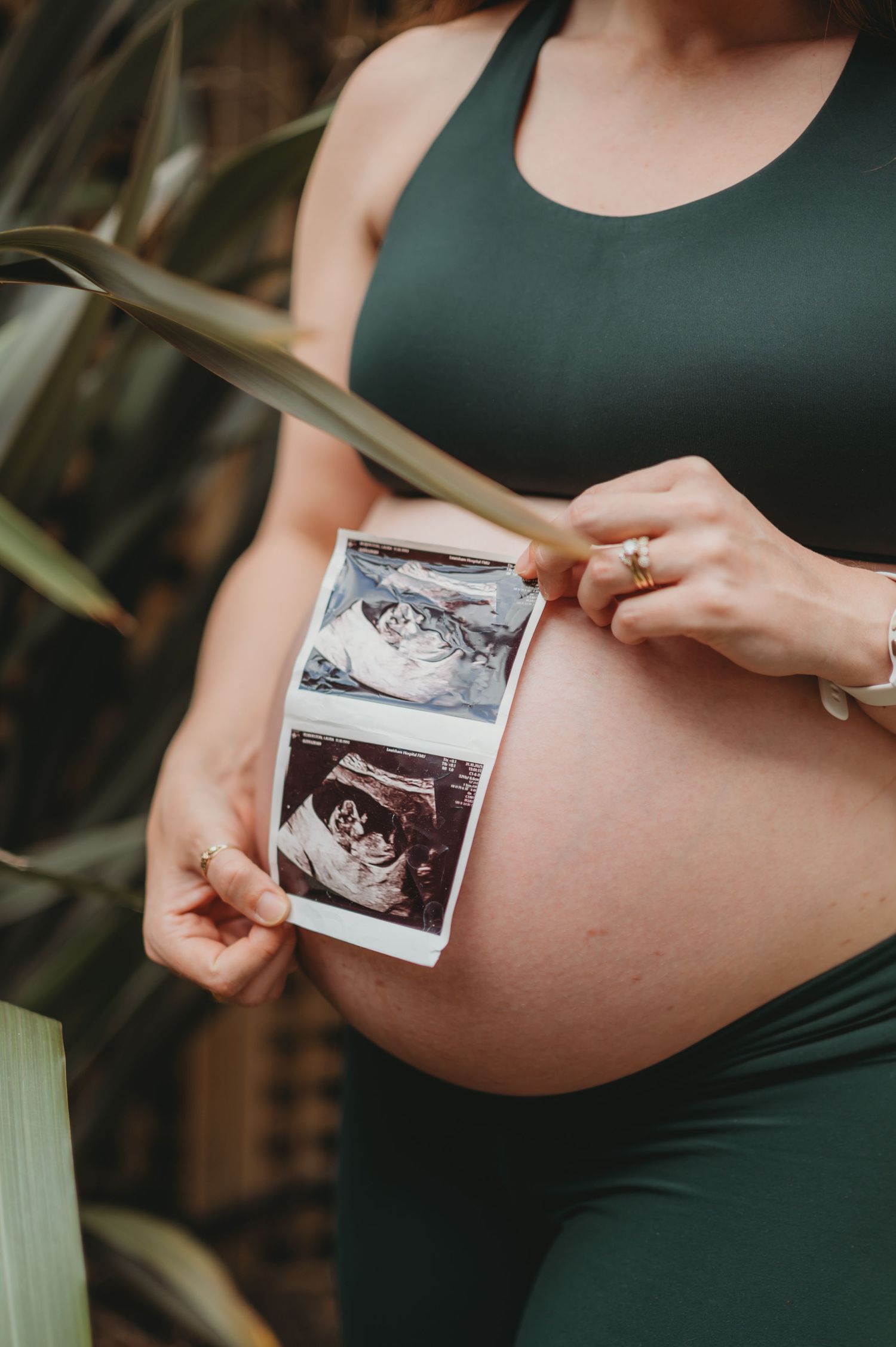 Pregnant woman in green outfit holding ultrasound photos against baby bump.