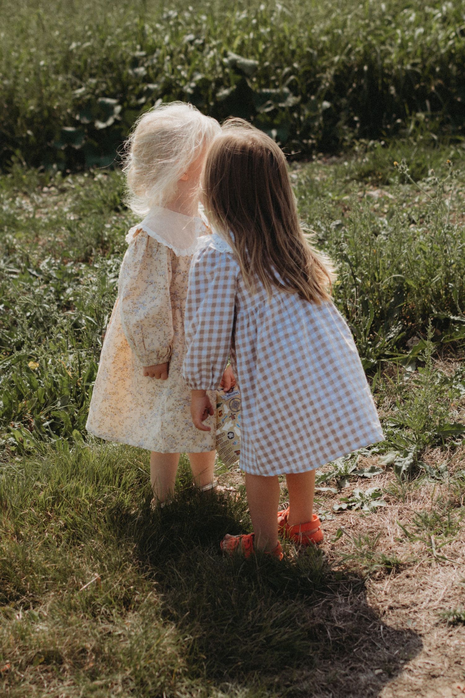 Two little girls in floral and gingham dresses standing together outdoors.