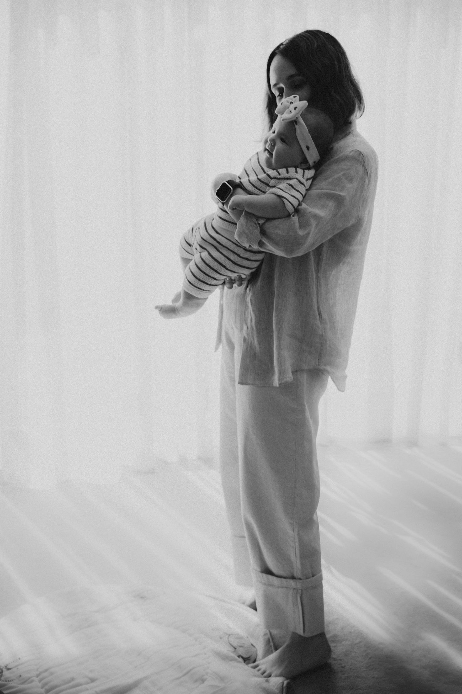 Black and white photo of a mother in linen pajamas tenderly holding her newborn baby.