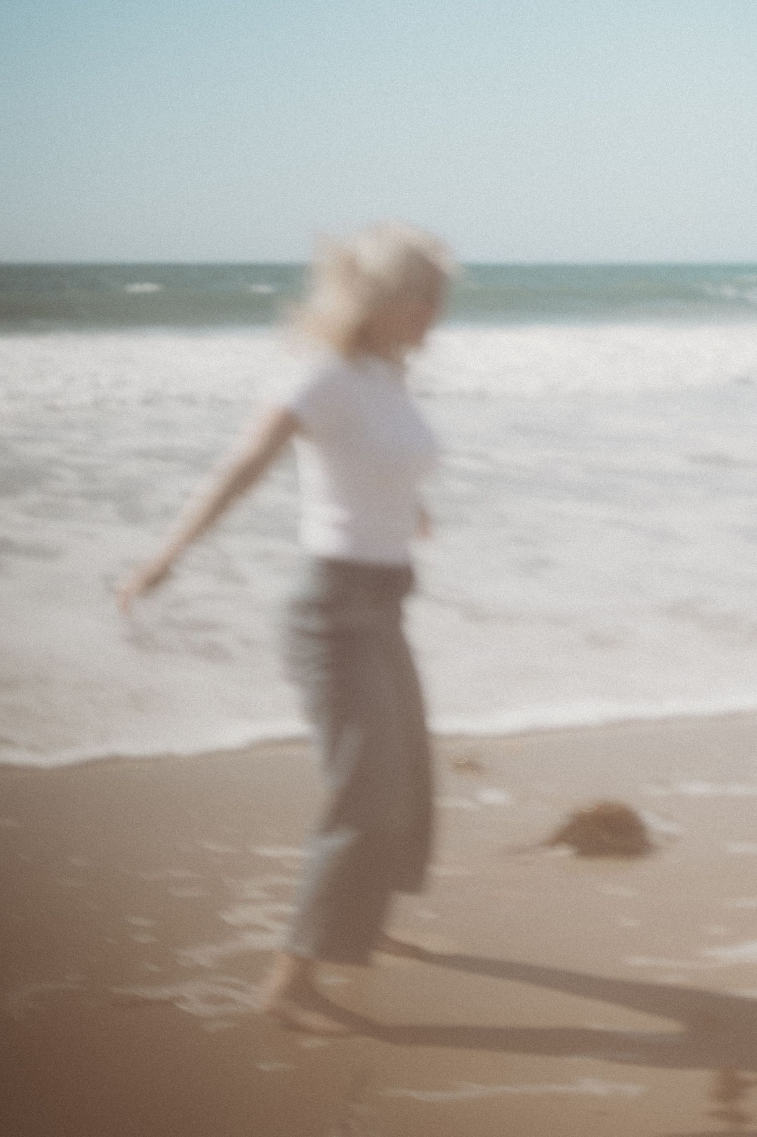 Artistic blurred motion shot of blonde woman in white tee dancing near ocean waves.
