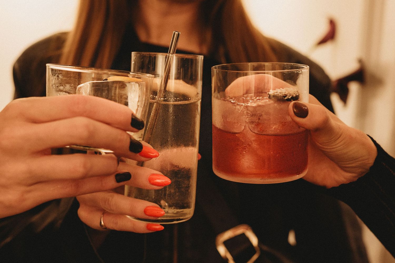 Close-up of hands with colorful nails holding cocktail glasses at a party.
