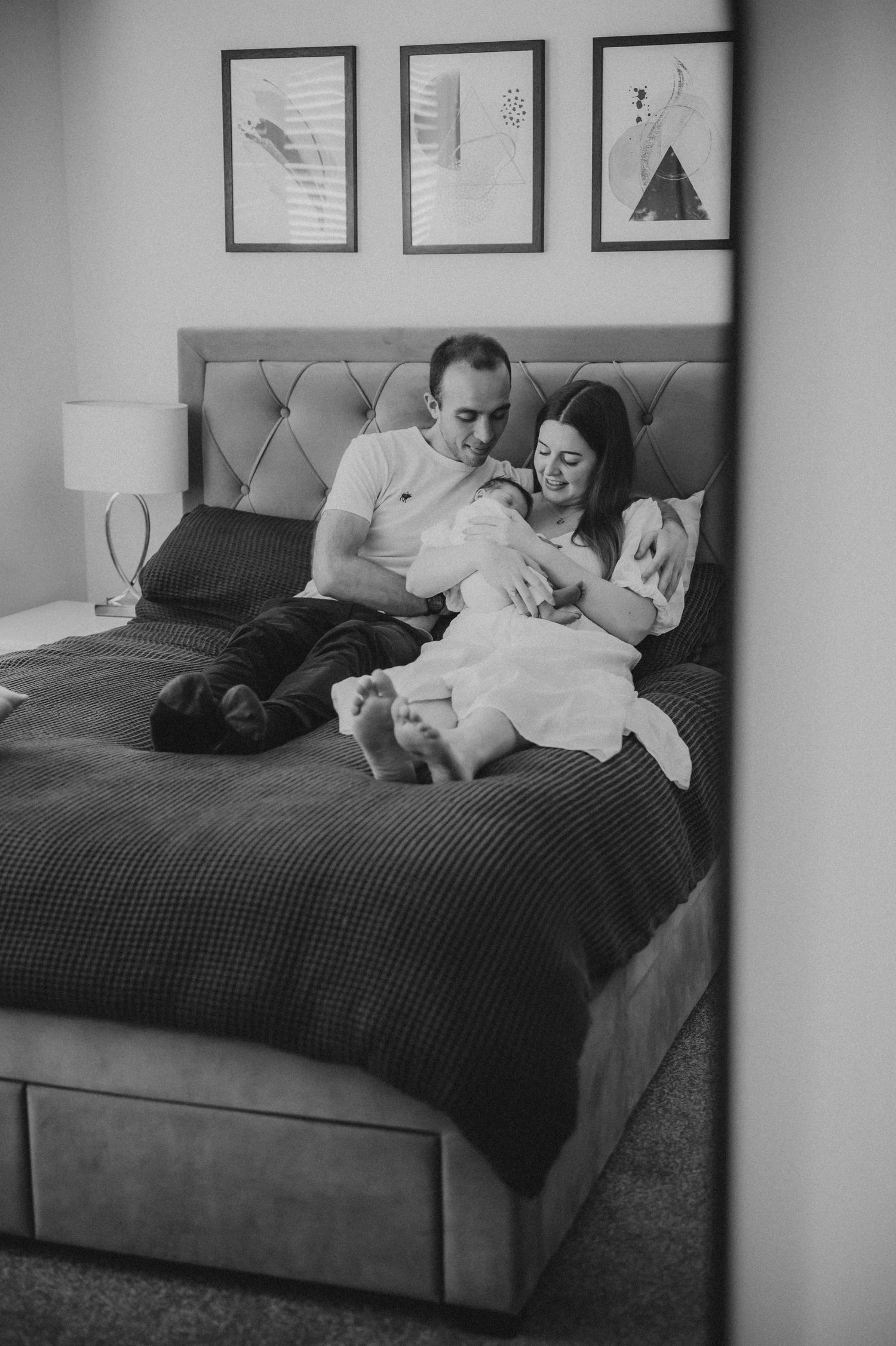 Black and white photo of couple relaxing on bed lovingly holding their newborn baby.