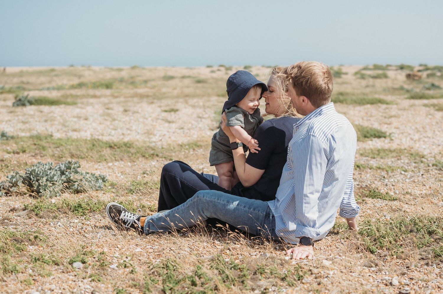 Two men sitting outdoors on rocky ground with young baby.
