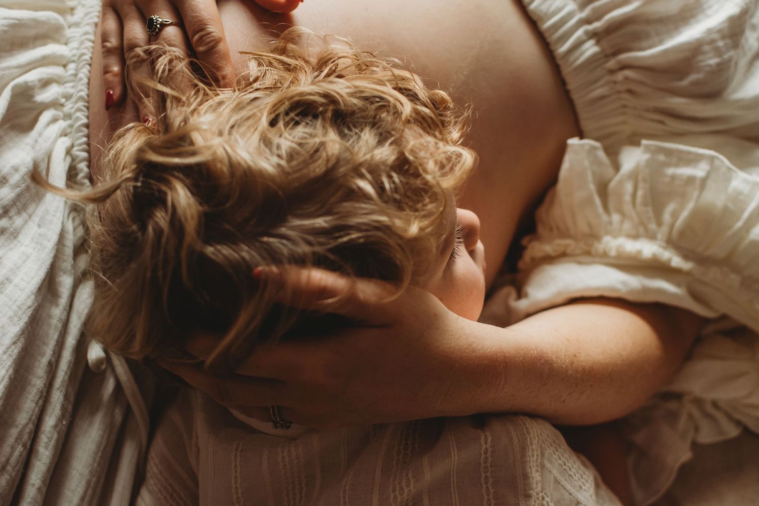 Overhead view of a pregnant woman with curly hair lying down gently holding her bare baby bump.