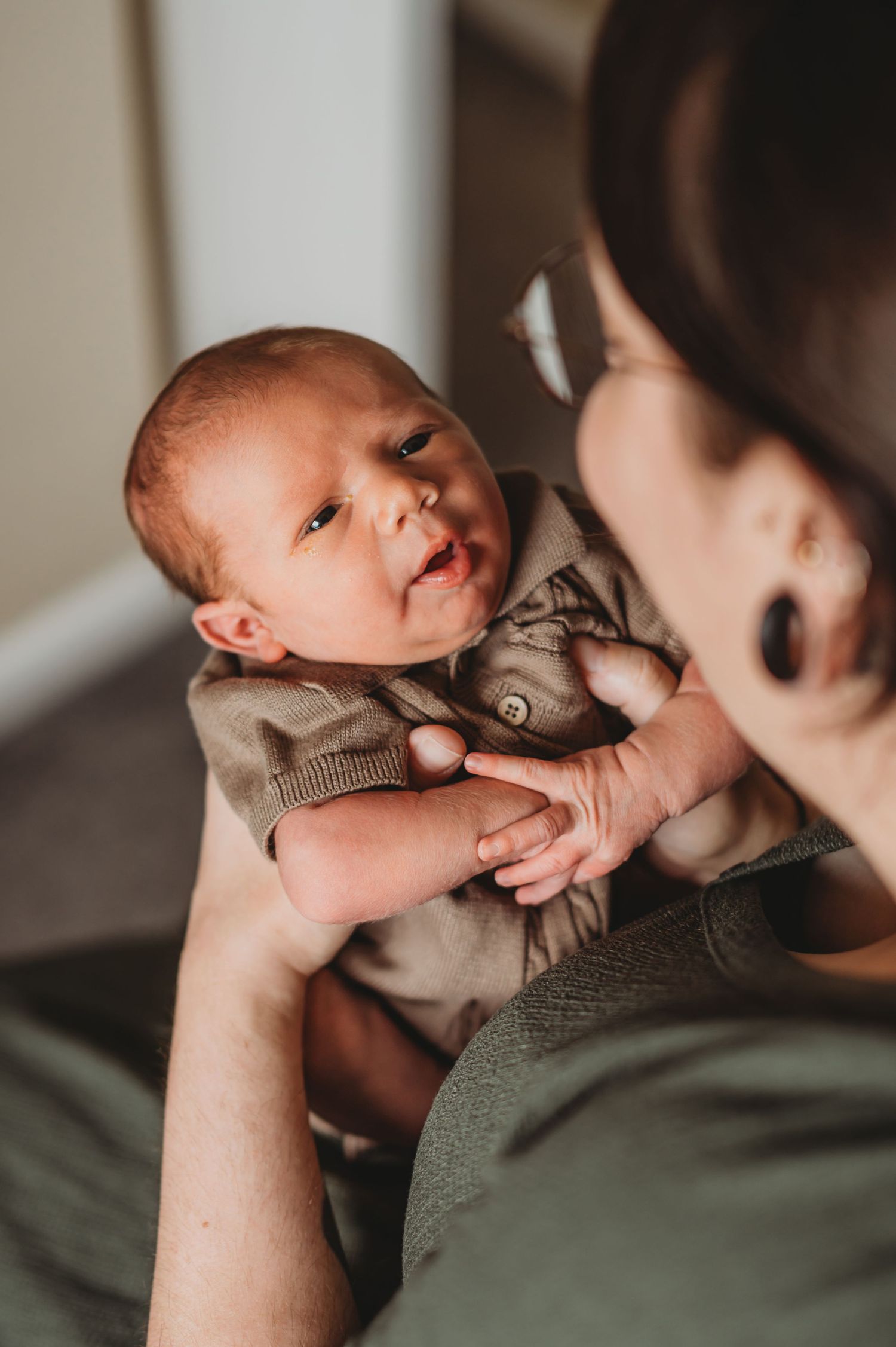 Mother gazing lovingly at her alert newborn baby dressed in a olive green outfit.