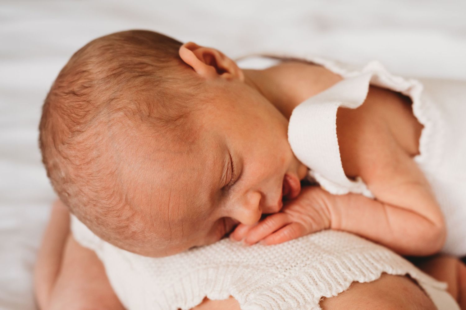 Peaceful sleeping newborn baby in white onesie resting on soft white blanket.