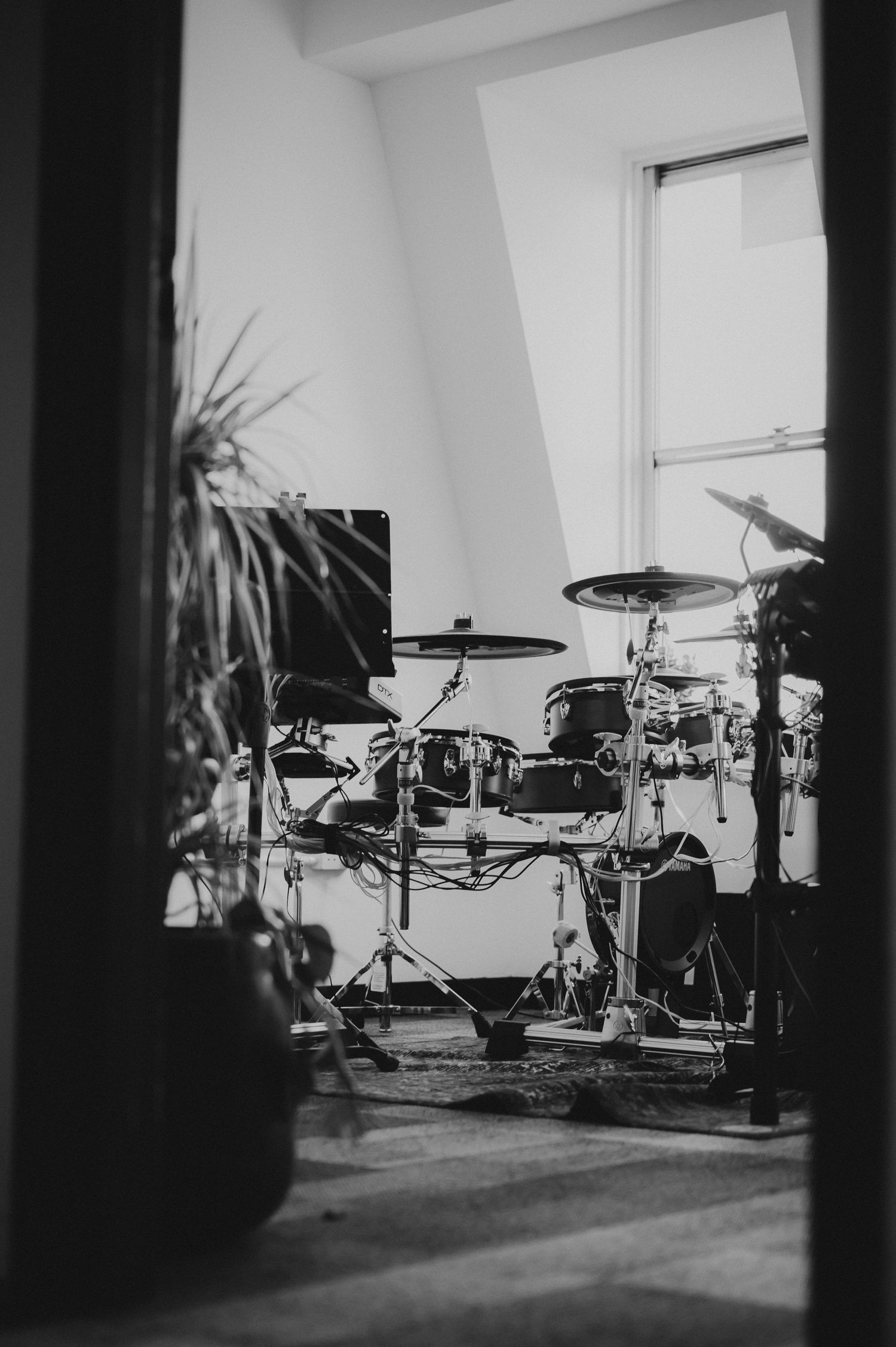 A black and white photo of a professional drum kit set up near a bright window in a music studio.