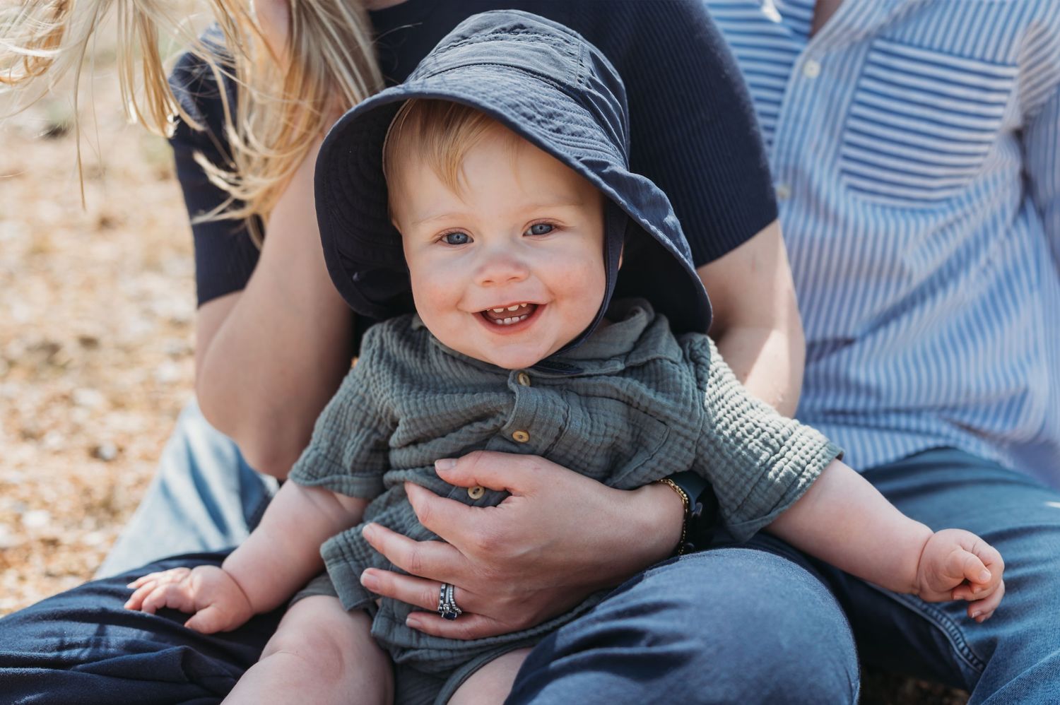 Happy baby in blue hat and green outfit smiling outdoors.