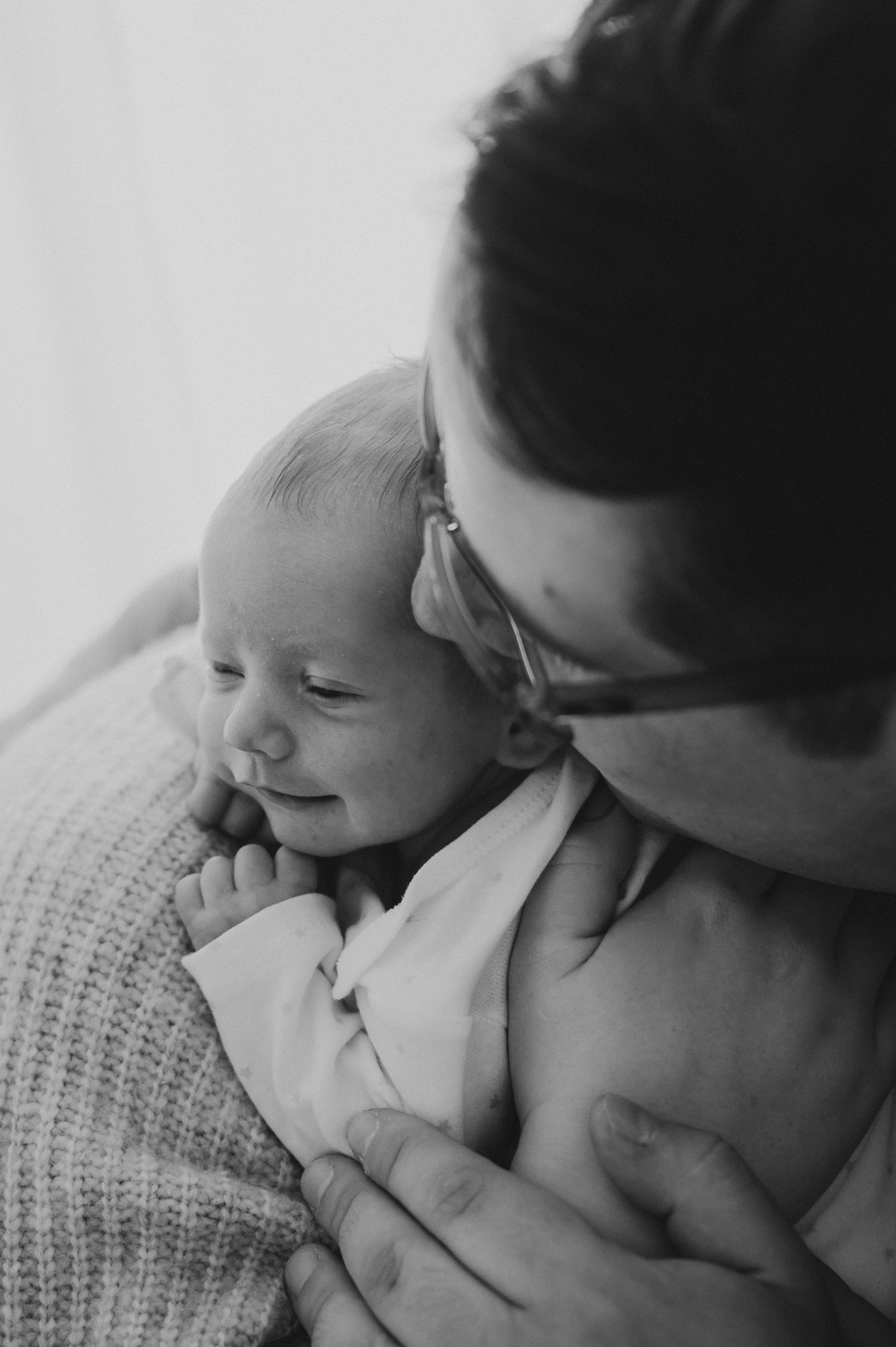 Black and white photo of father in glasses tenderly holding smiling newborn baby.