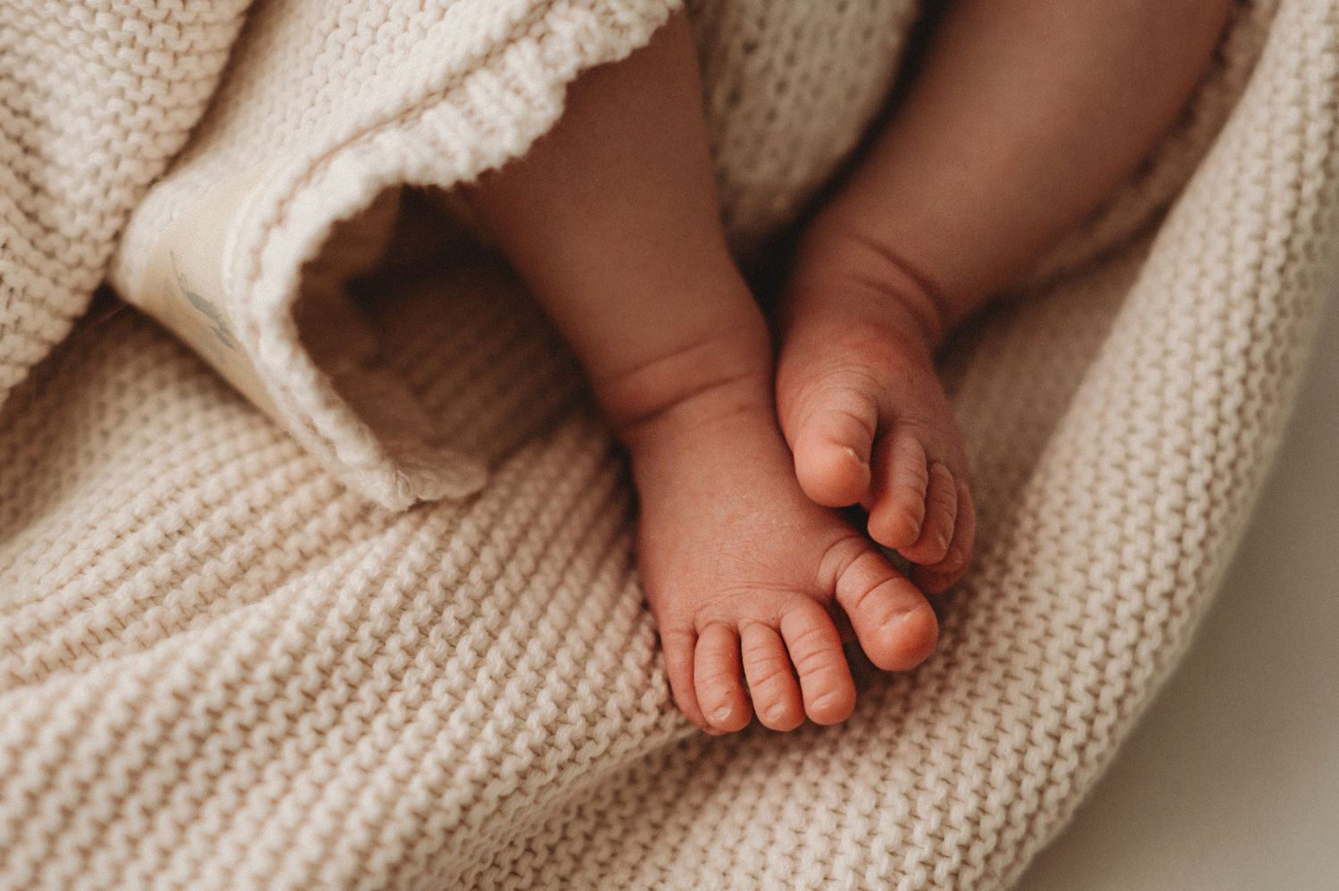 Close-up of tiny newborn baby feet wrapped in a soft cream knitted blanket.