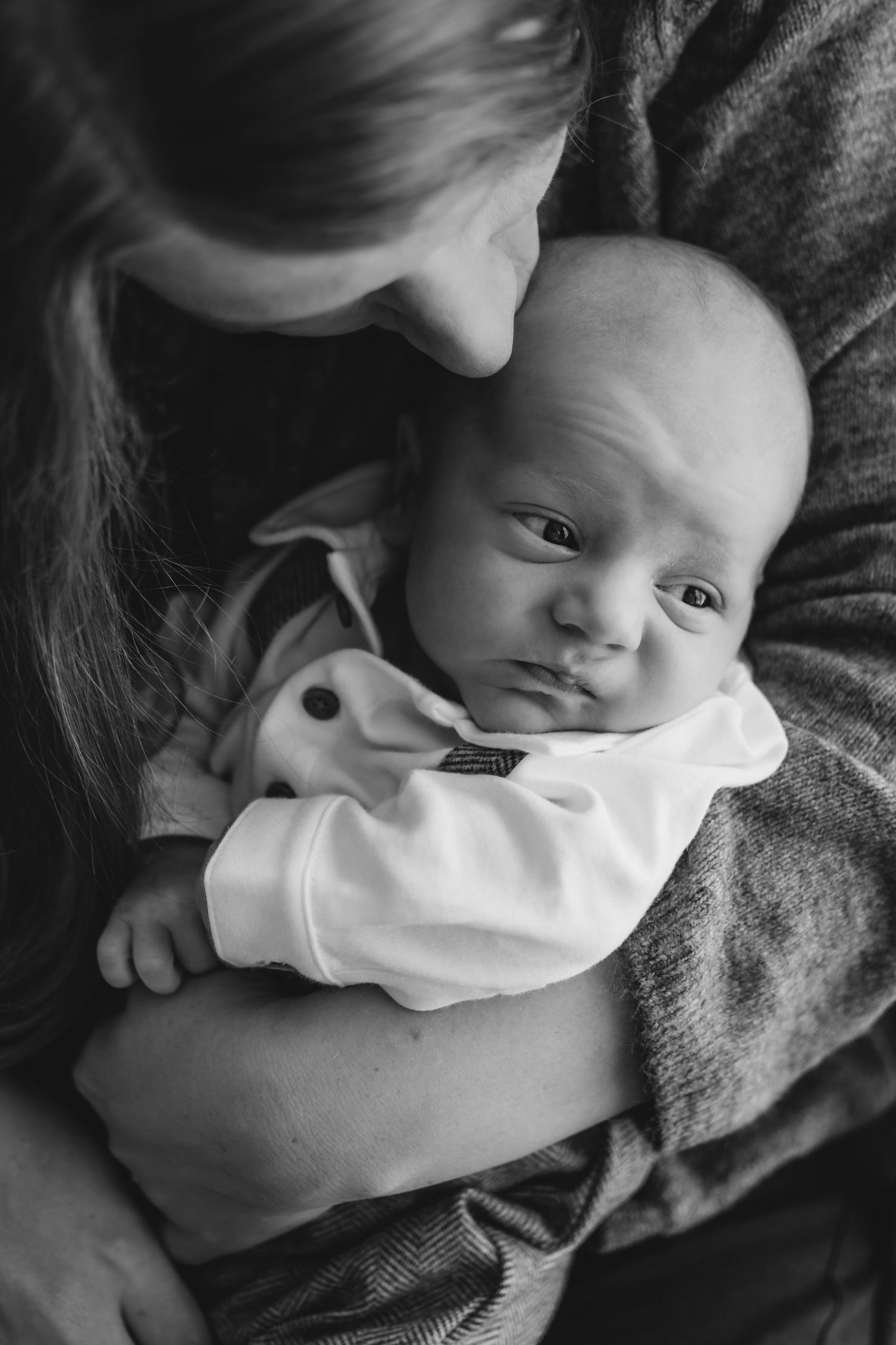 Black and white portrait of a mother holding her wide-eyed newborn baby close.