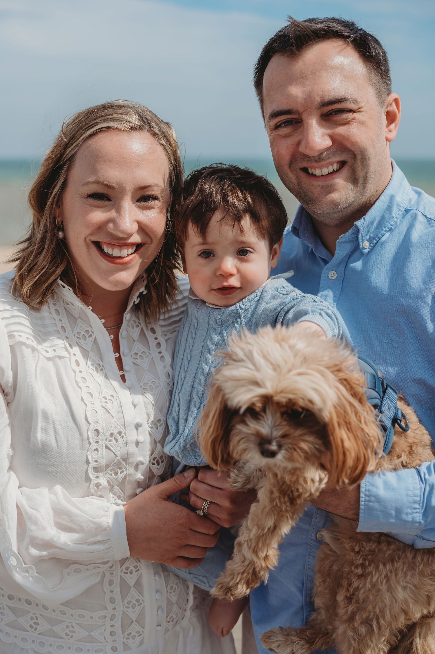 Happy young family with a toddler and fluffy dog smiling together on a sunny beach.