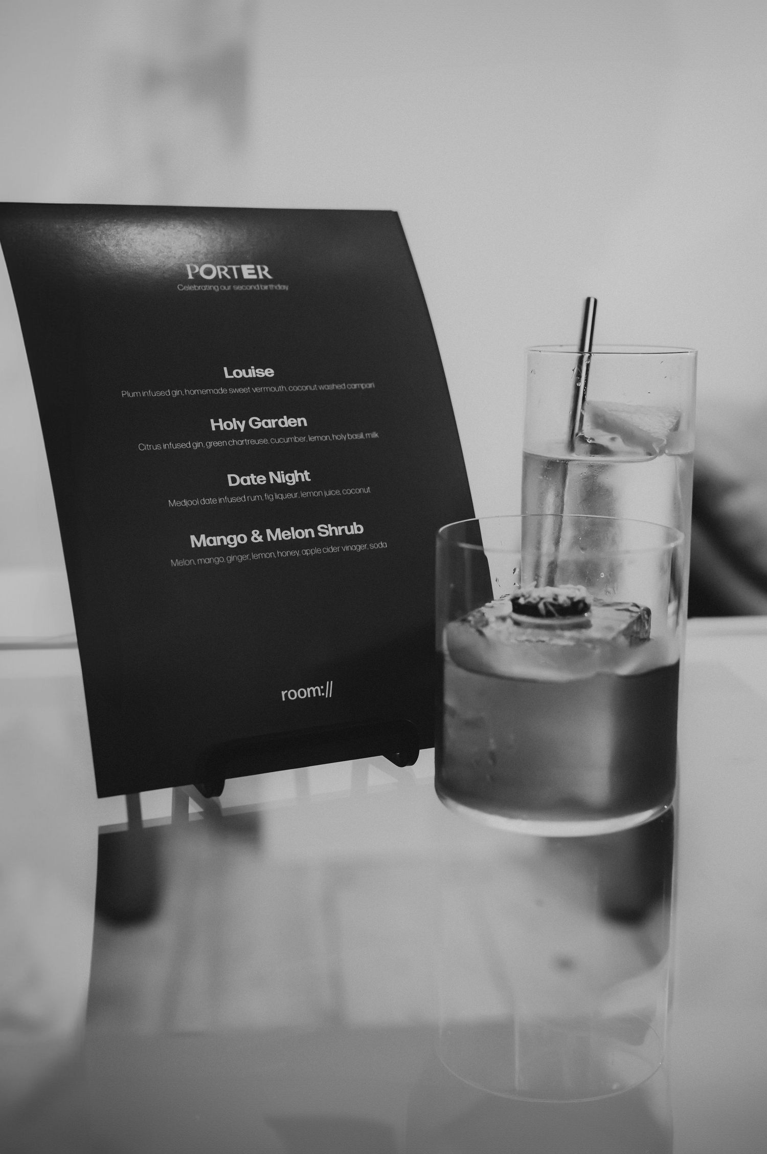 Porter cocktail menu card beside two elegant drinks with ice and metal straws on a table.