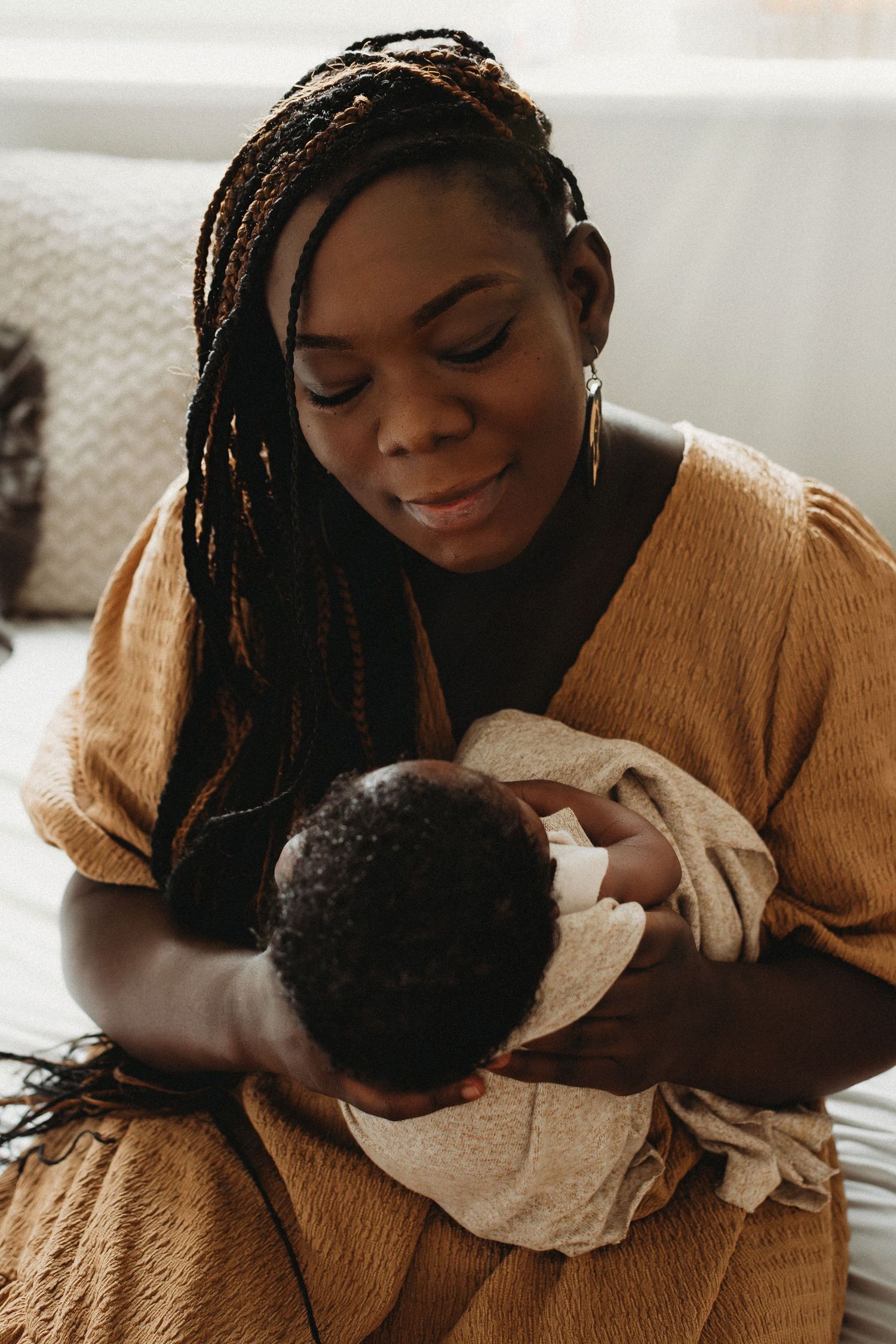 A mother in a golden dress gently cradles her sleeping newborn baby in her arms.