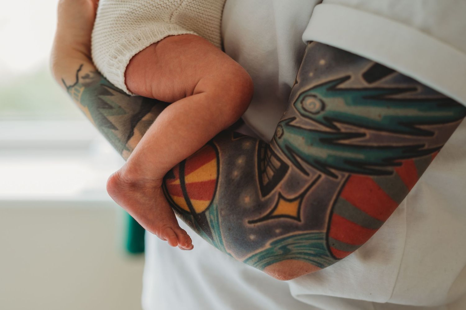 Newborn baby cradled in the arm of a parent with colorful tattoo sleeve.
