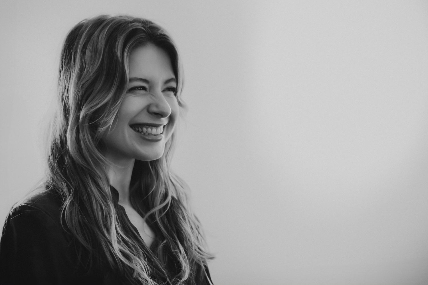 Black and white portrait of a laughing blonde woman against a light background.