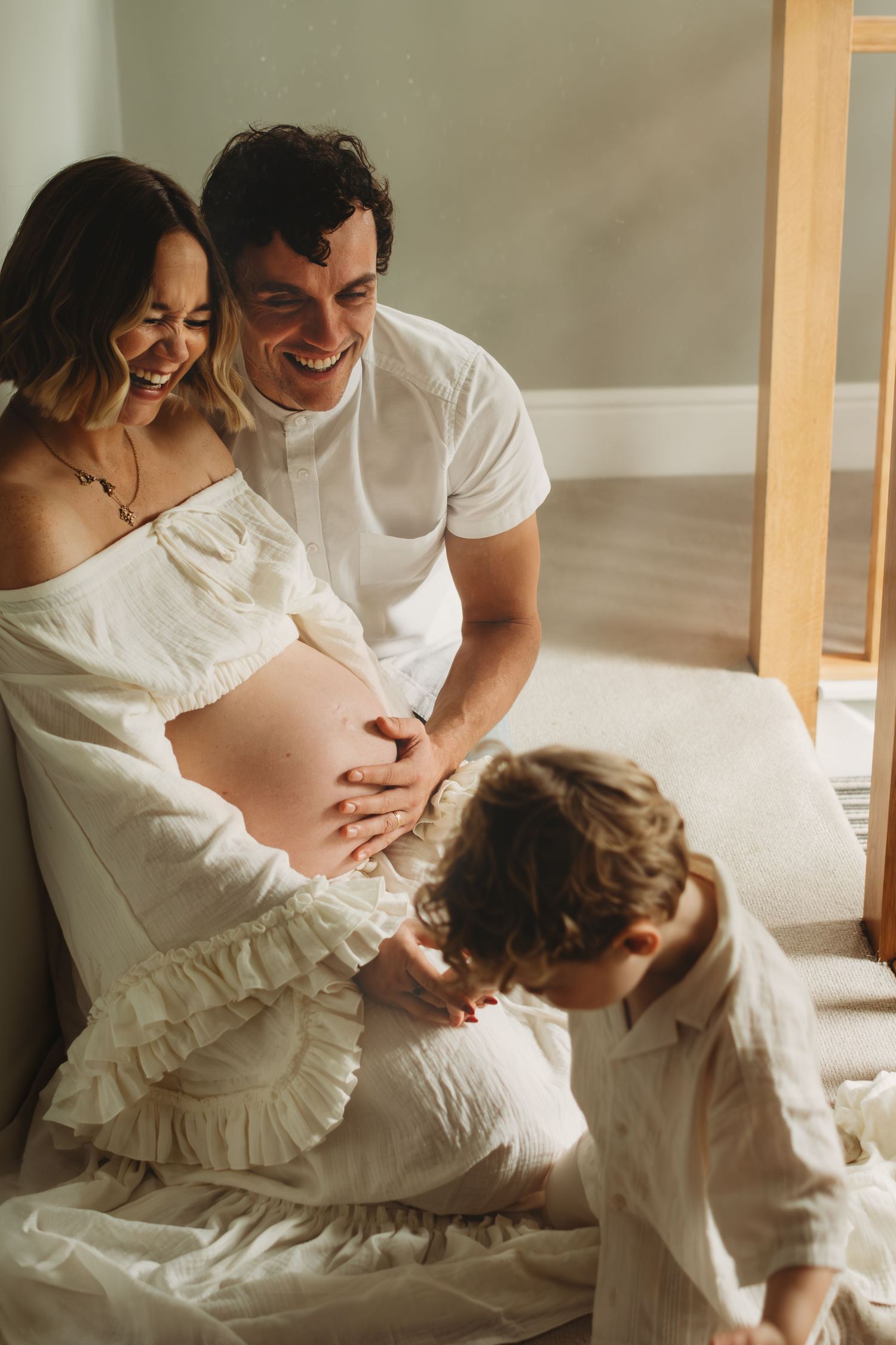 Happy family shares a joyful moment as child touches pregnant mothers belly on a bed.