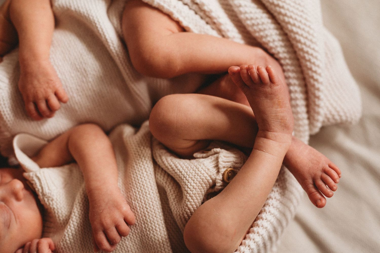 Close-up of four tiny newborn baby feet resting on a soft cream knit blanket.