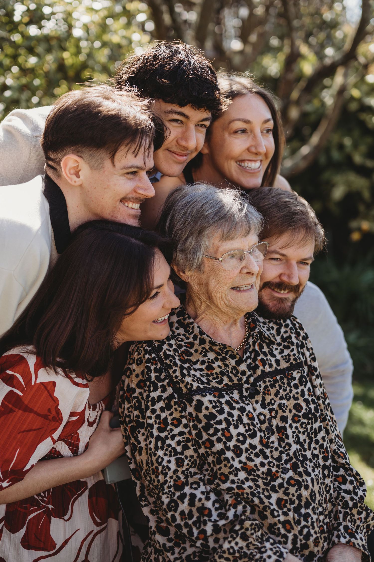 Multigenerational family of six smiling together outdoors in warm sunlight.