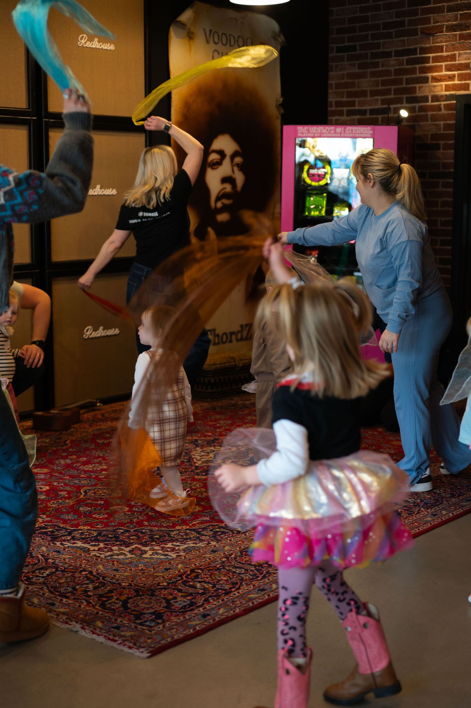 Young girls in colorful tutus dance and twirl with ribbons during a lively music-themed children's event.