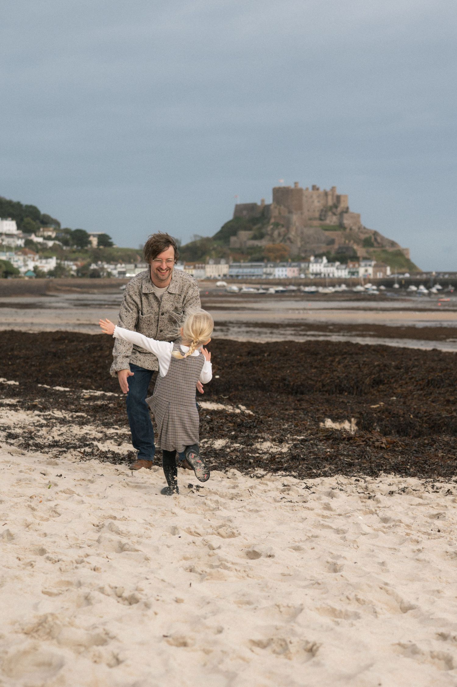 Woman and child playing on a sandy beach with a historic castle on a hill in the background.