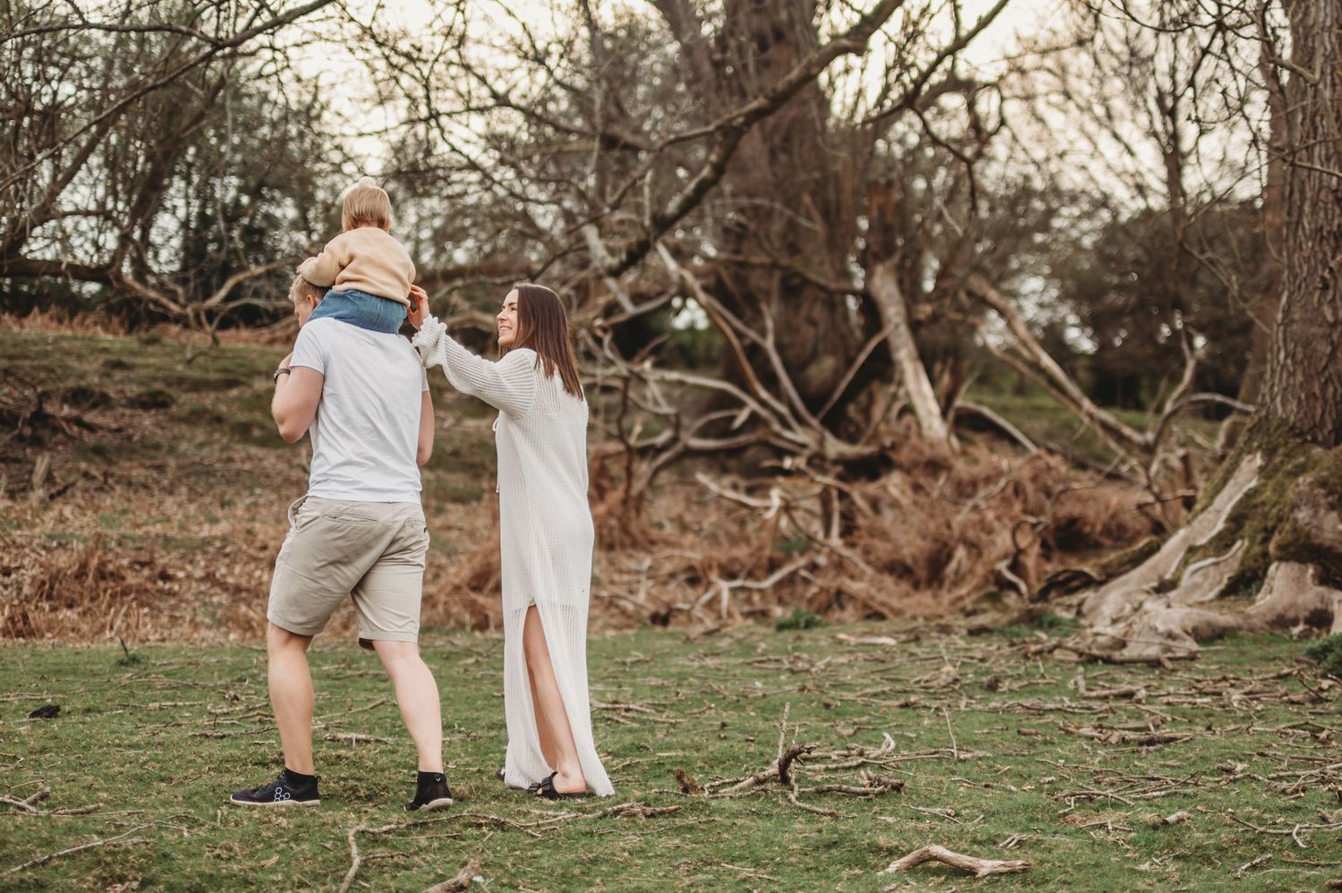 Parents lifting toddler joyfully in a woodland clearing outdoors.