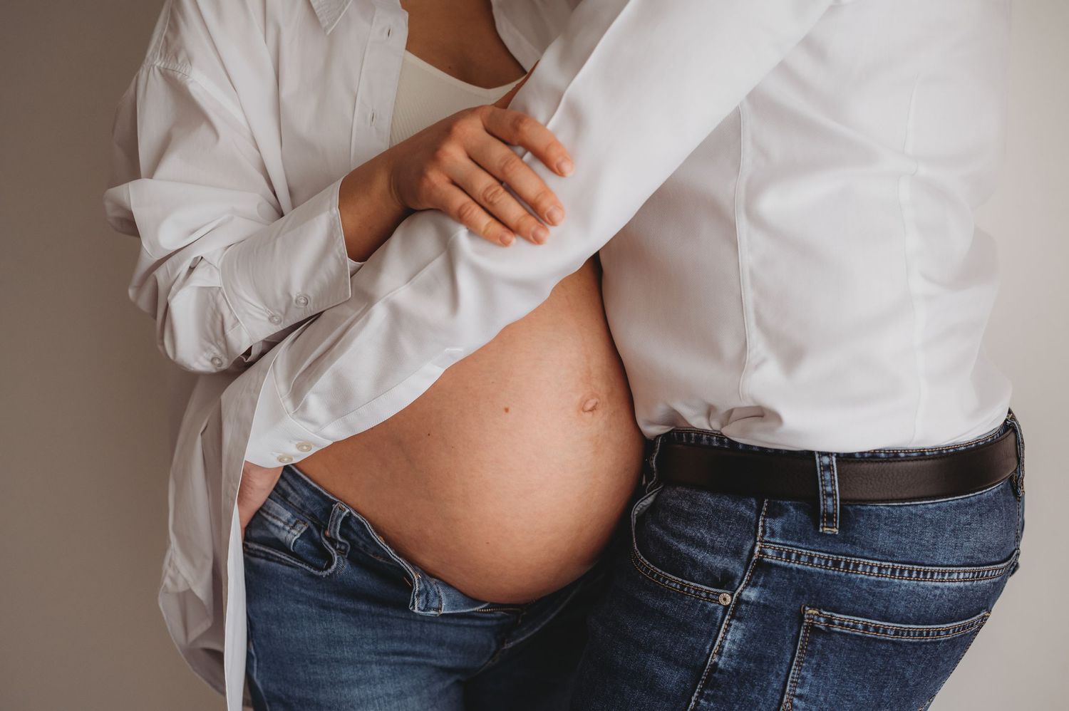 Couple in white shirts and jeans showing pregnant belly bump together.