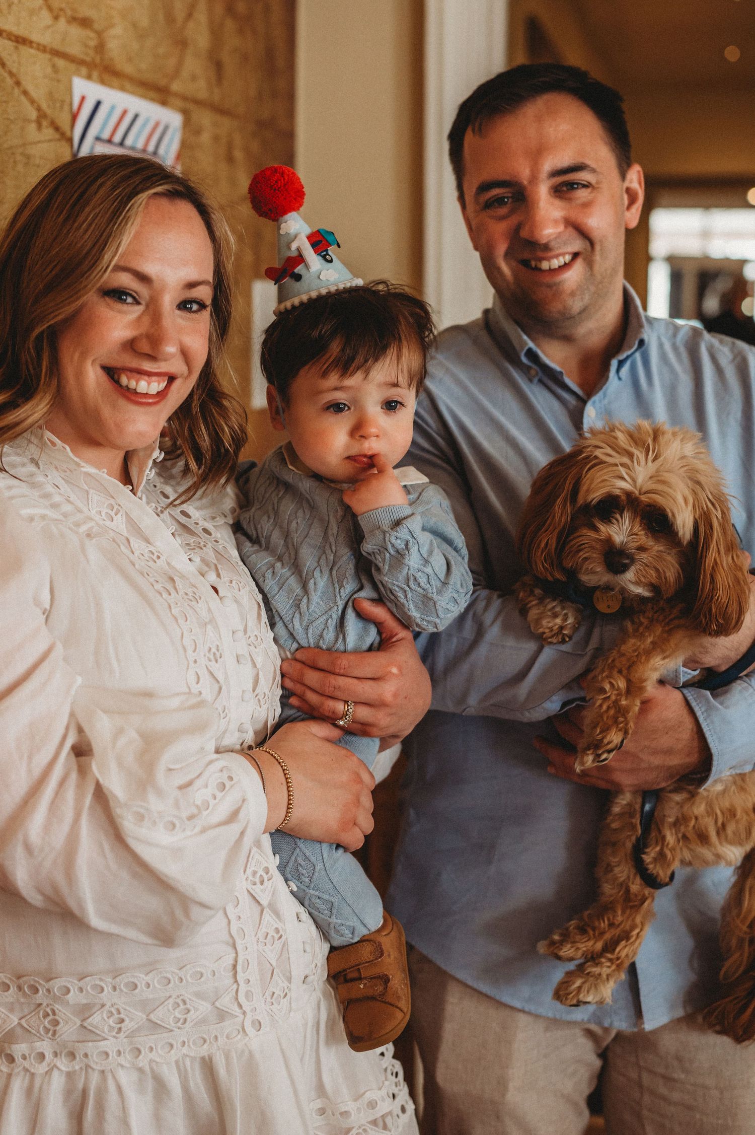 Smiling family with baby in birthday hat and fluffy cavoodle dog.
