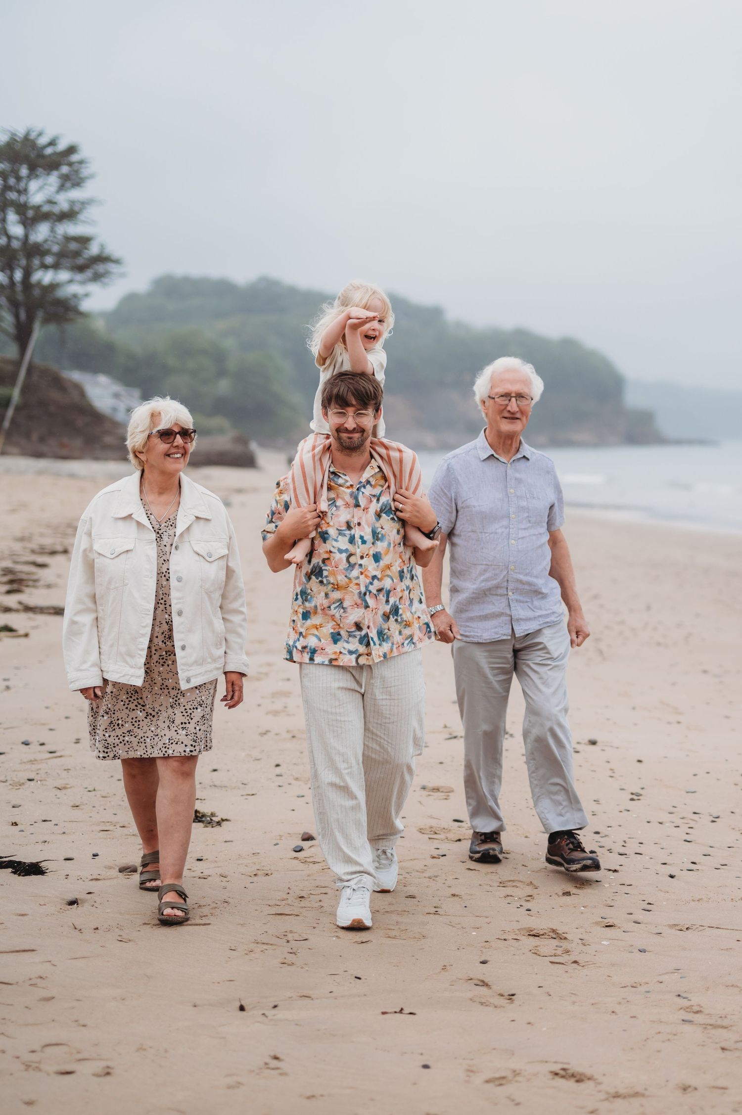 A multigenerational family walks together on a sandy beach on a misty day.
