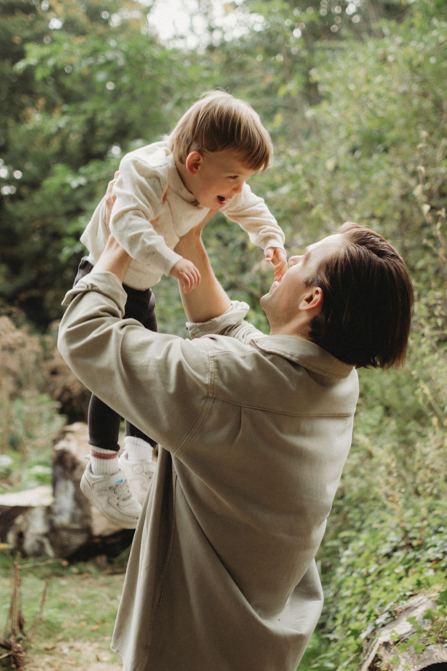 A parent lifts a laughing toddler high in the air during a fun outdoor moment in nature.