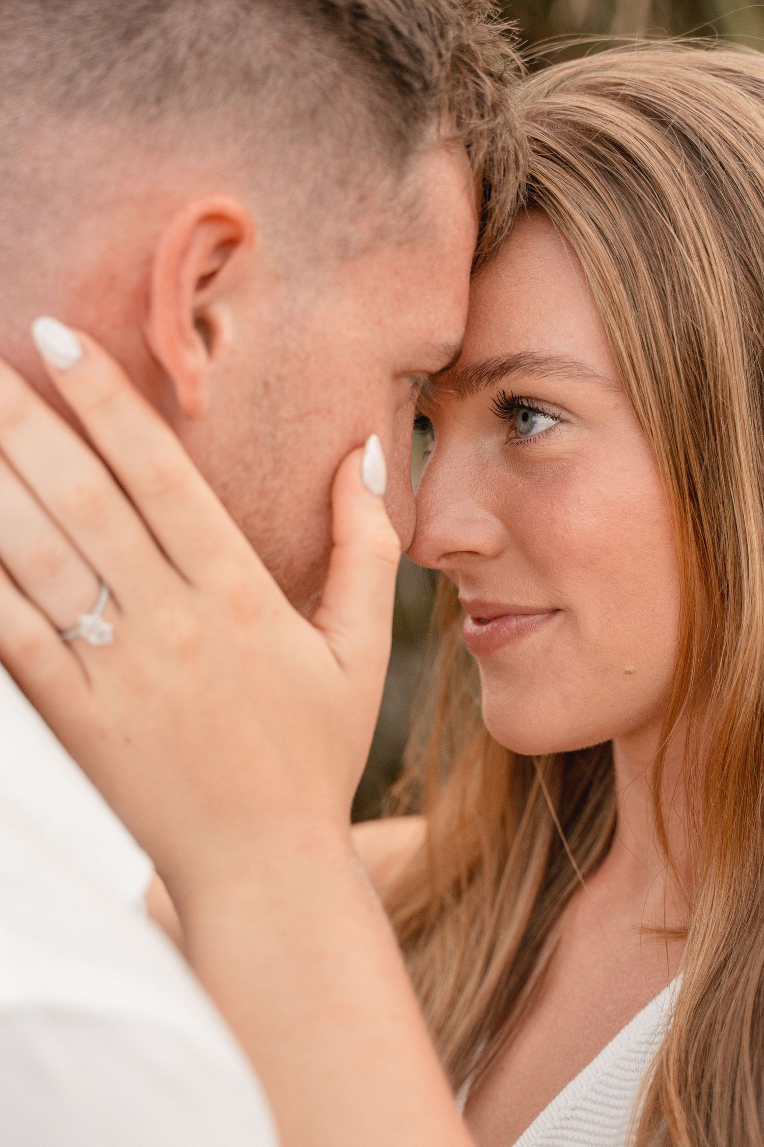 Close-up of a couple touching foreheads tenderly, woman wearing an engagement ring, sharing a romantic moment.