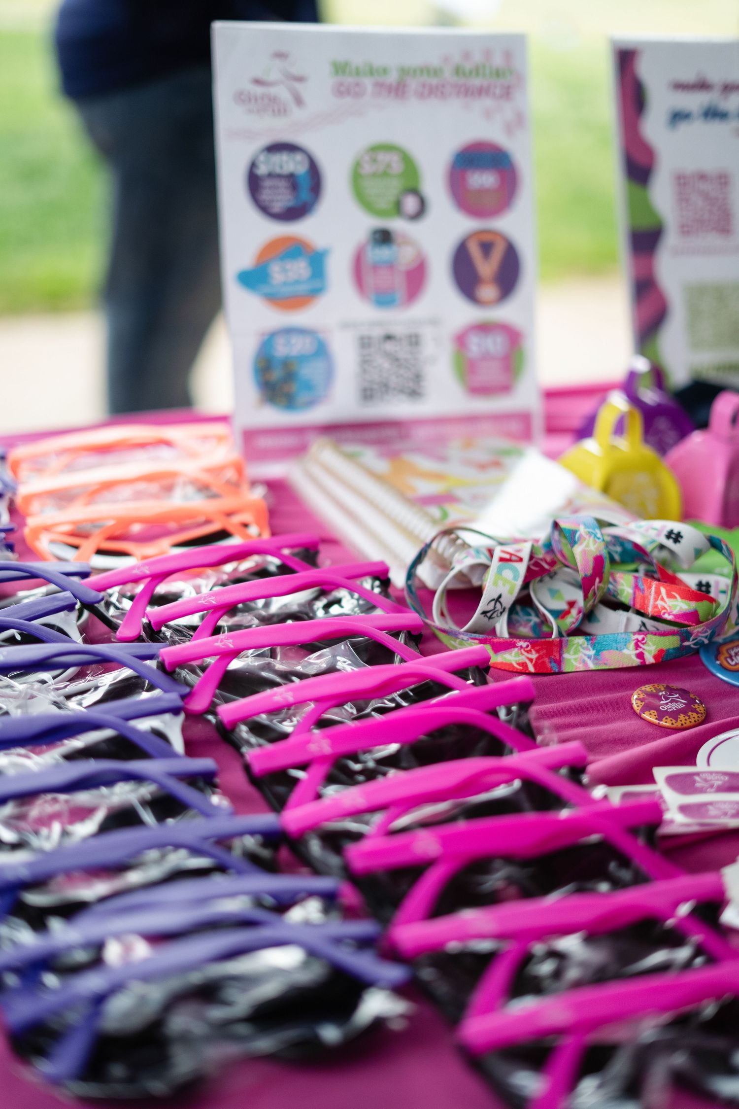 Pink sunglasses and colorful race medals displayed on a purple table at an outdoor 5K charity run event.