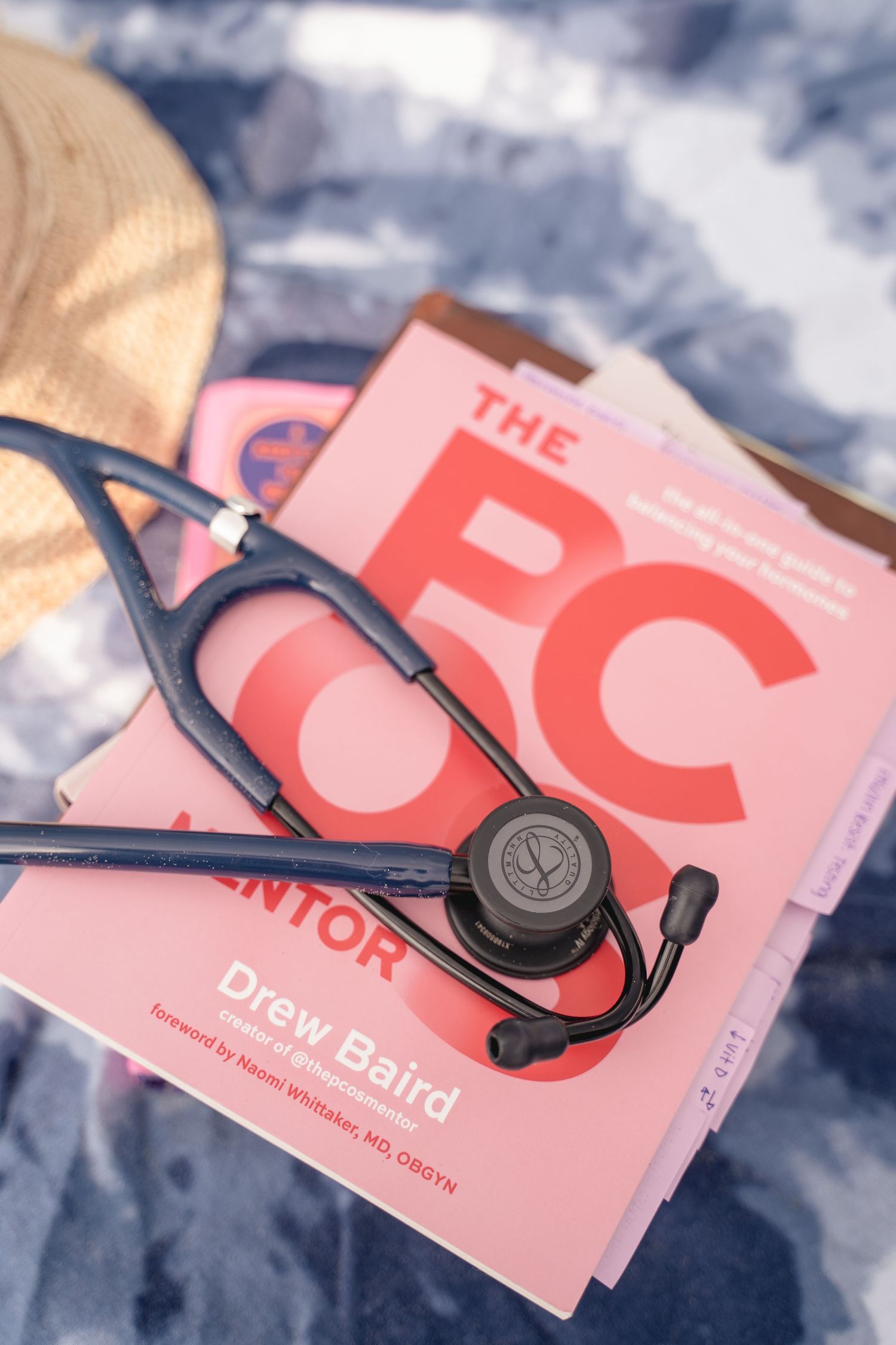 A stethoscope rests on pink medical books including The PC Mentor by Drew Baird on a blue surface.