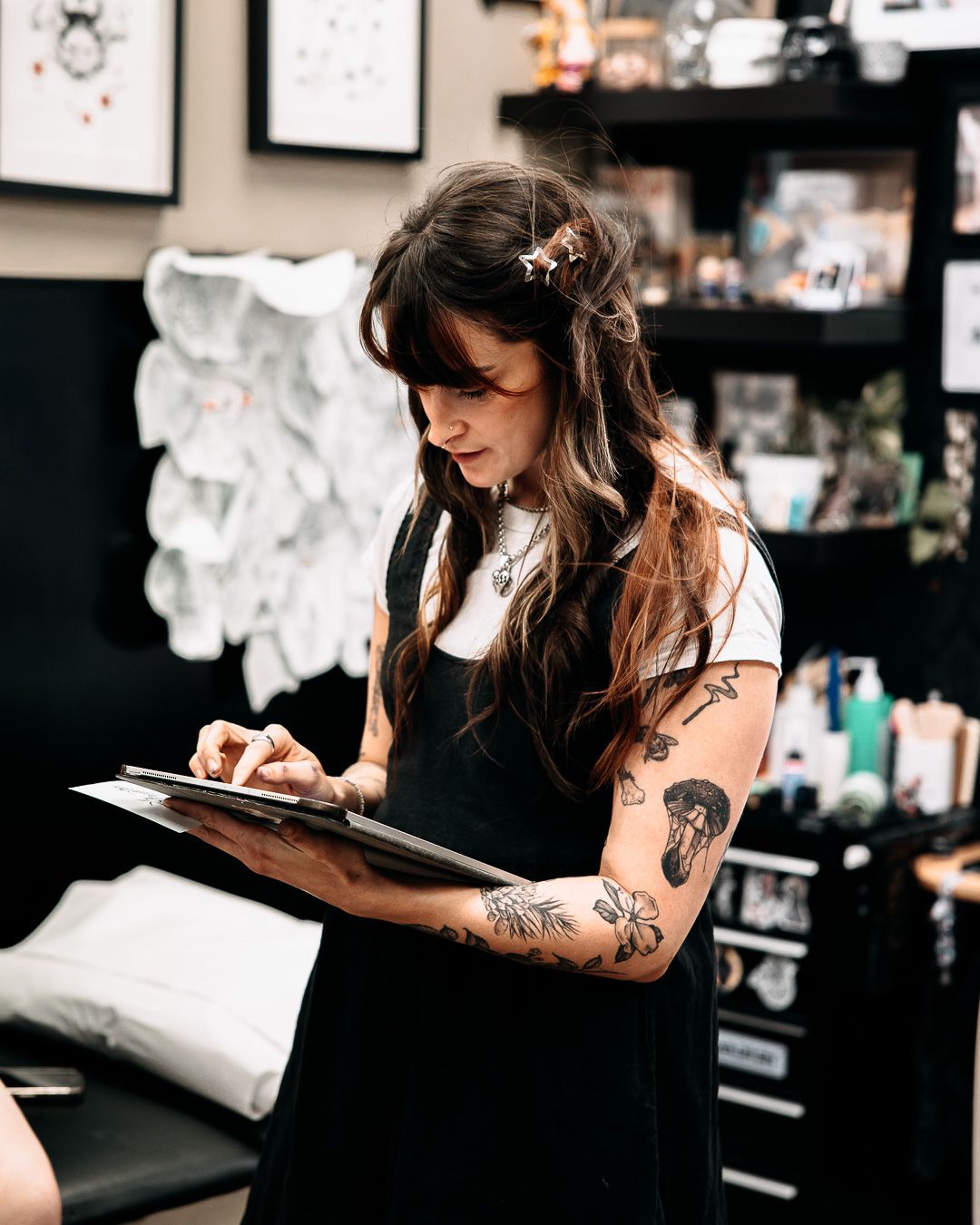 Tattooed female tattoo artist reviewing designs on clipboard in a professional tattoo studio.