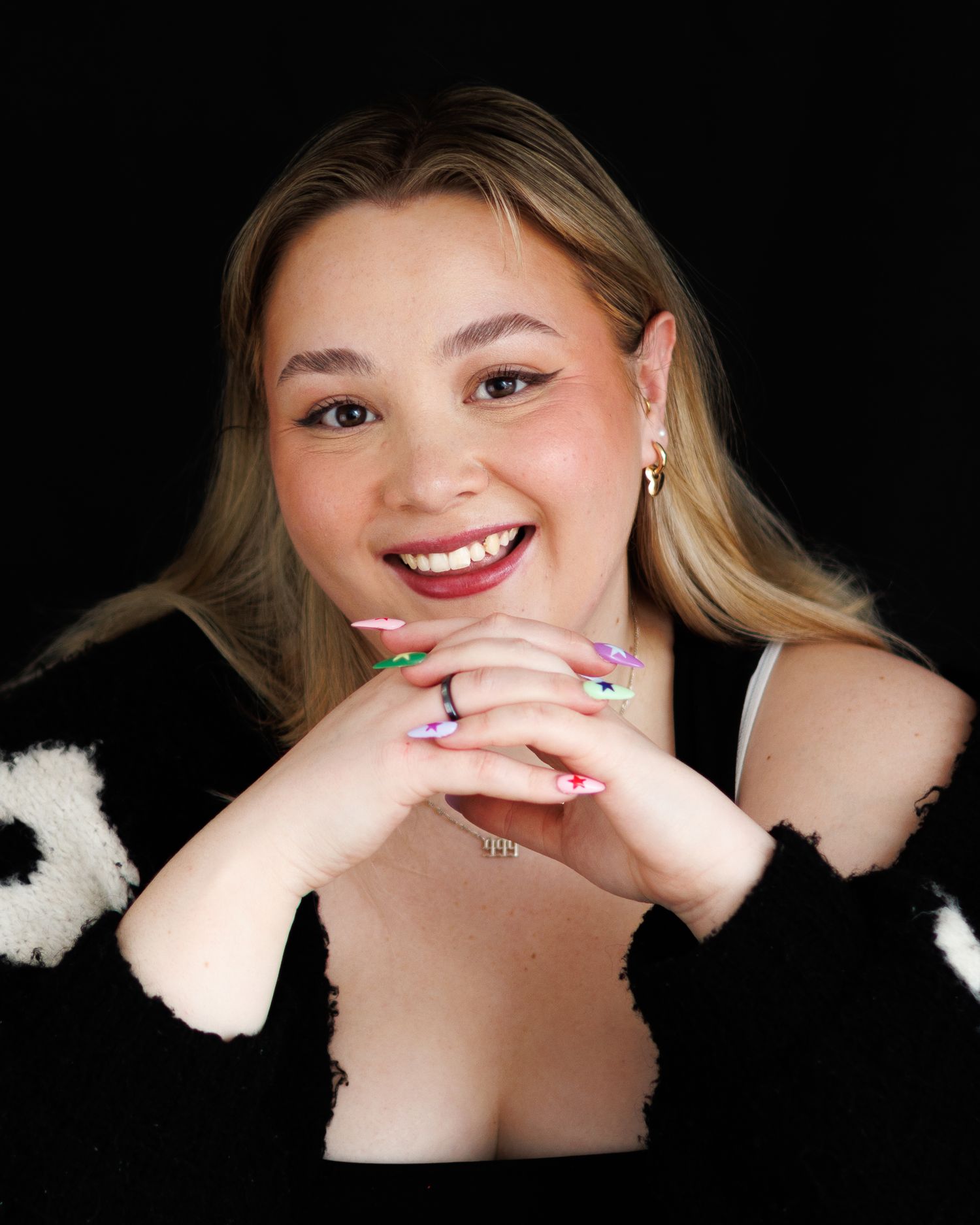 Smiling blonde woman with colorful nails wearing black and white floral cardigan.