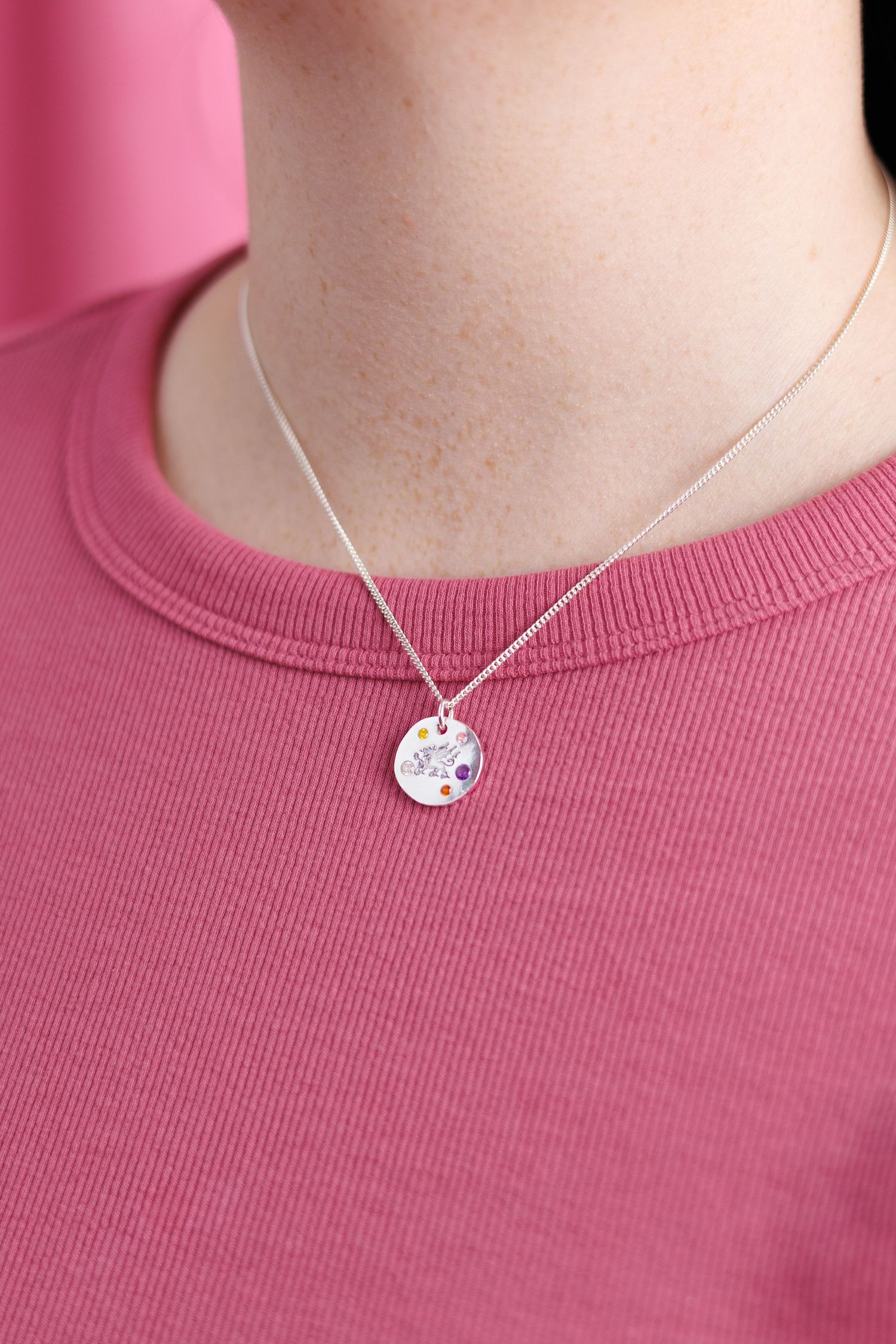 Silver disc pendant necklace with colorful gemstones on woman in pink ribbed top.