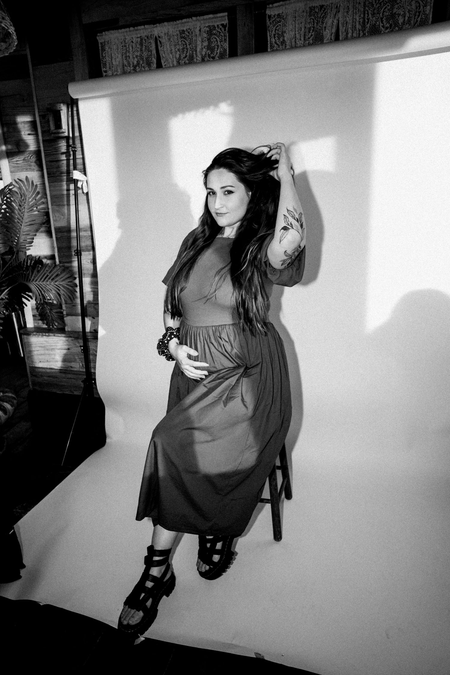 Black and white photo of a pregnant woman posing in a studio, wearing a midi dress and strappy heels.