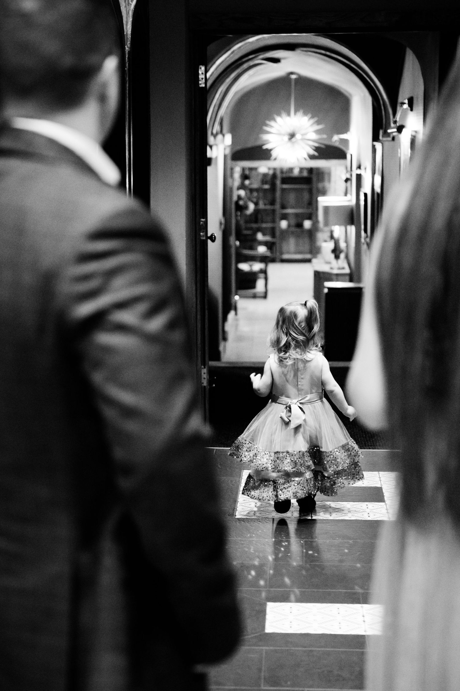 Black and white photo of a flower girl in a tulle dress walking through an arched doorway at a wedding.