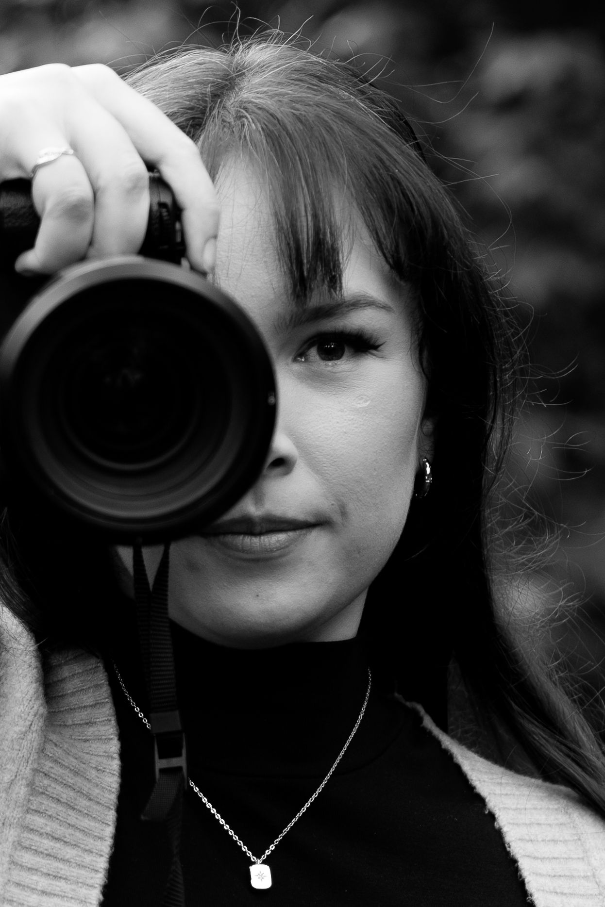 Black and white close-up of a female photographer holding a camera up to her eye outdoors.