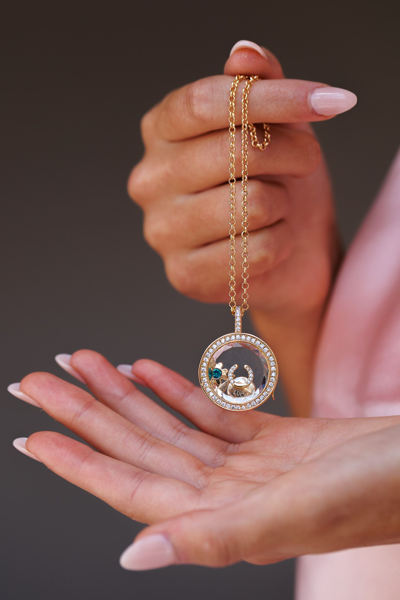 Woman holding a gold chain necklace with a circular diamond and gemstone Cancer zodiac pendant.