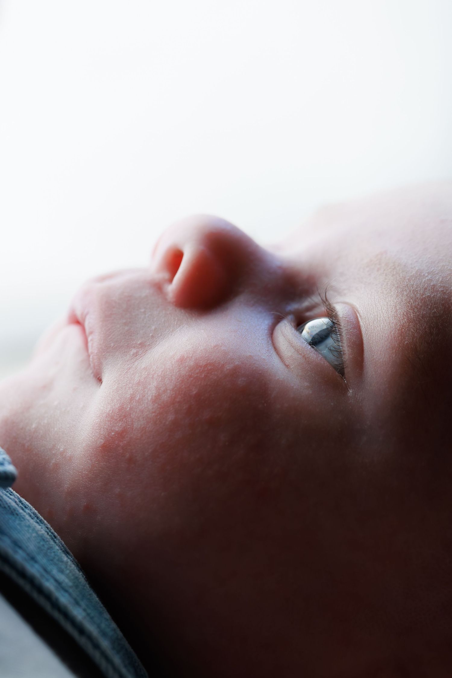 Close-up portrait of a newborn baby with blue eyes looking upward against a soft white background.