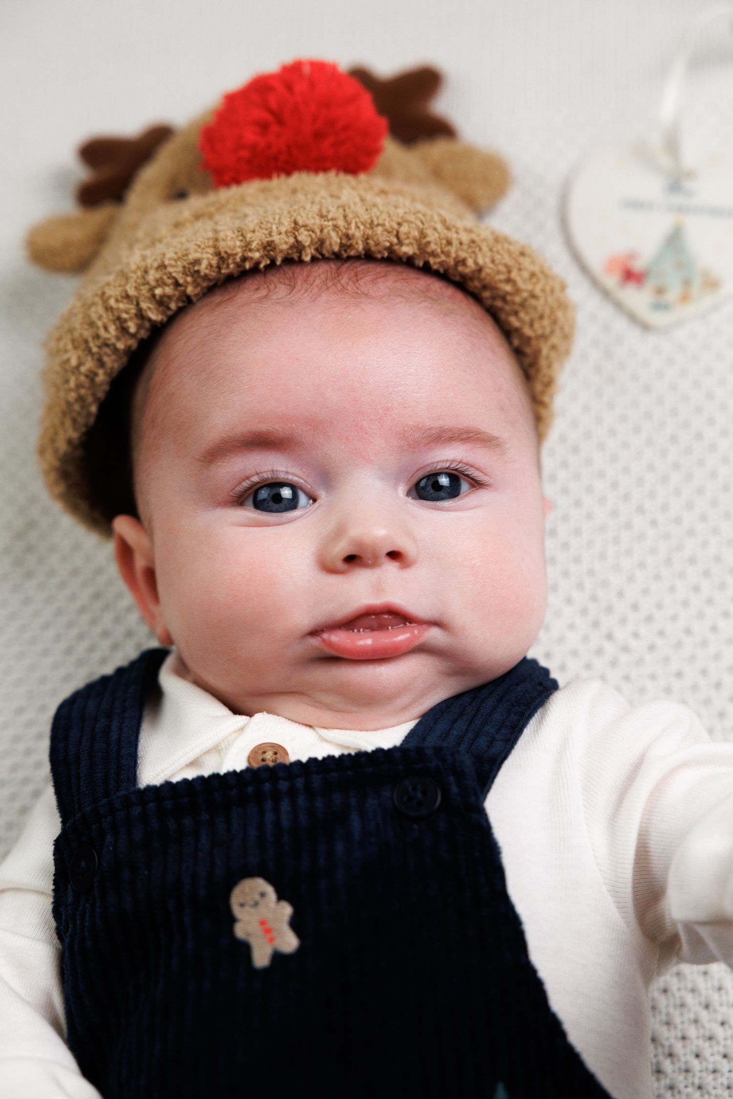 Adorable baby wearing a reindeer Christmas hat and navy dungarees with a gingerbread man badge.