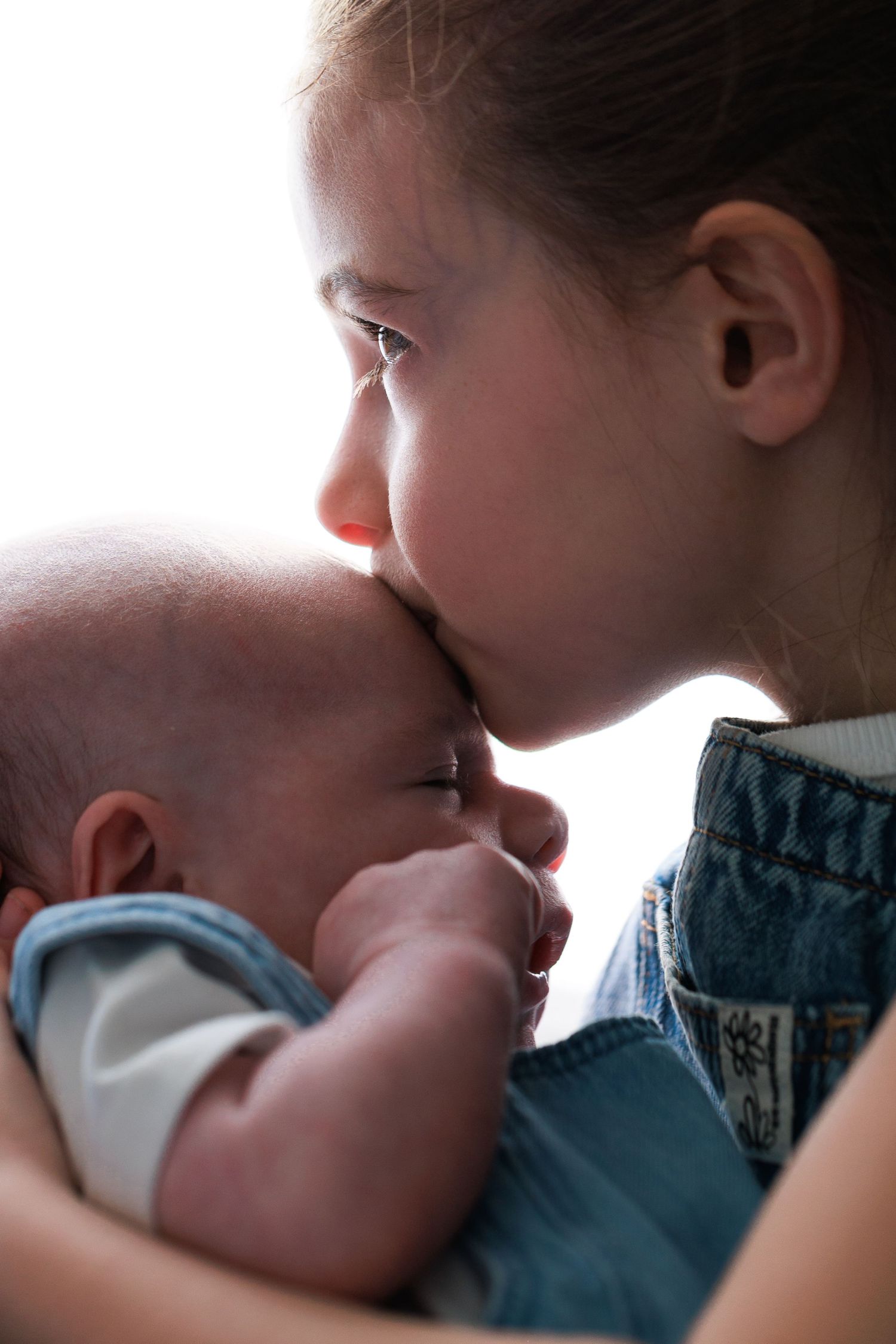 Young girl tenderly kissing a sleeping newborn baby she holds carefully in her arms.