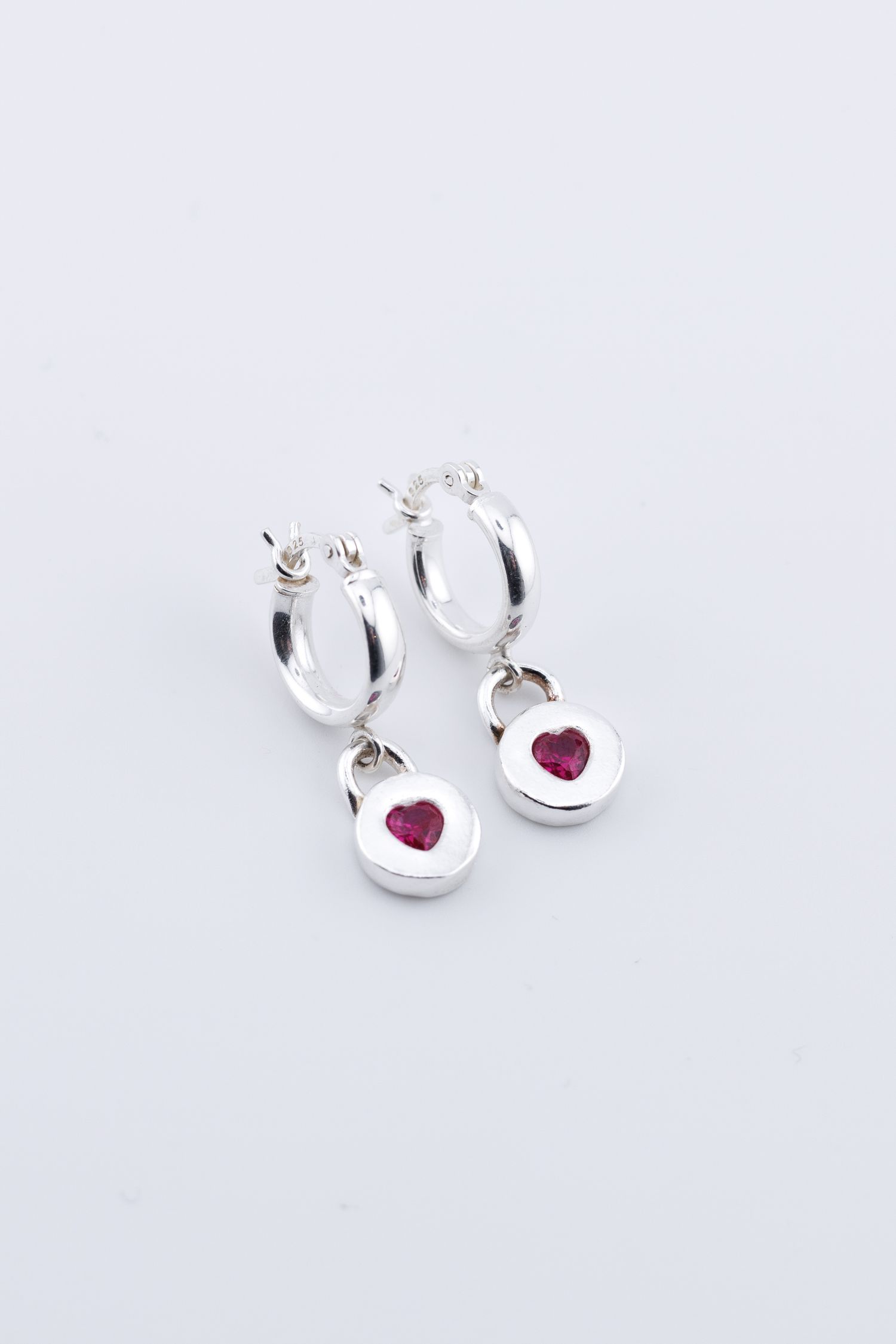 Silver hoop earrings with round pink heart crystal charm pendants on white background.